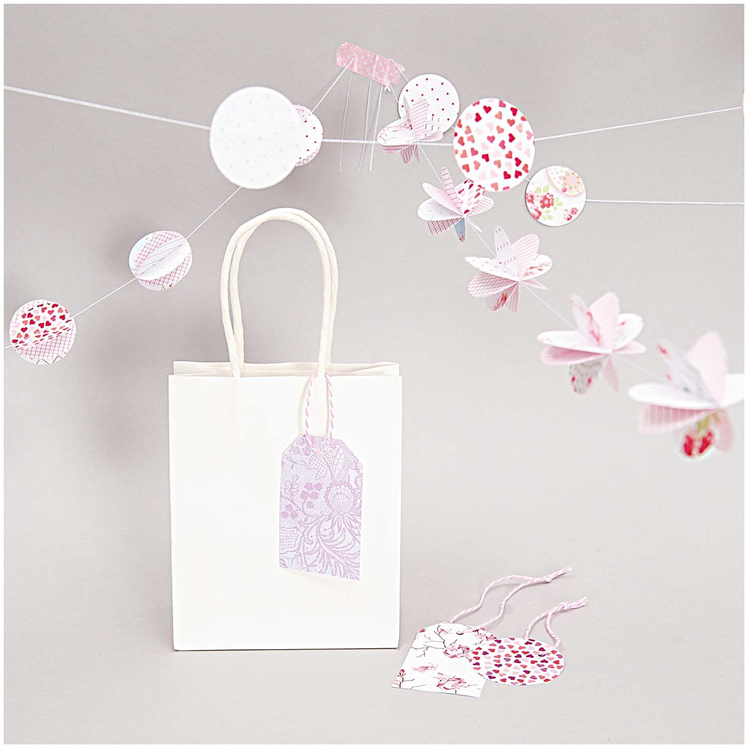 Papiertüte weiß von Rico Design mit dekorativen Anhängern und hängenden Papierornamenten.