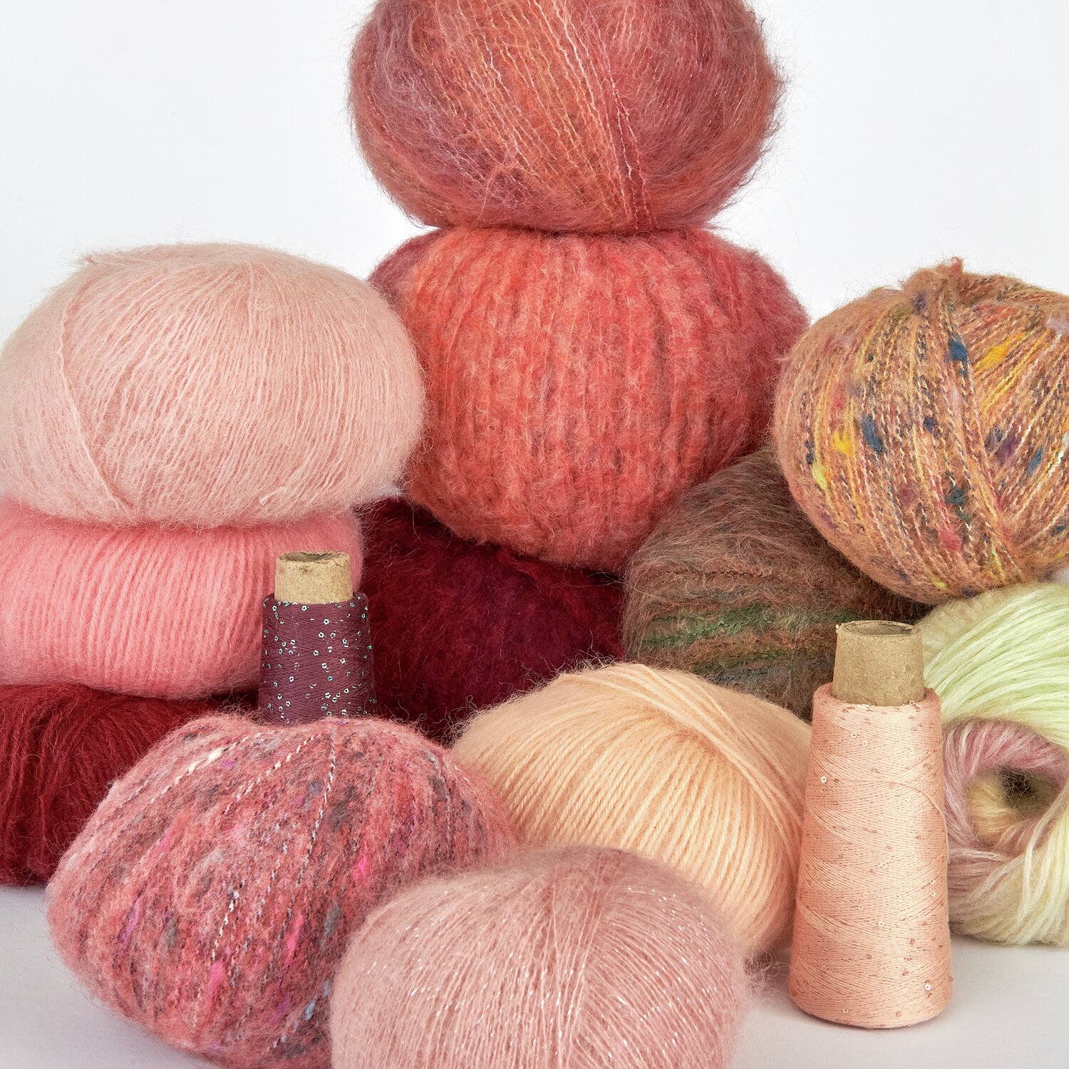 Lovewool No. 21 Herbst-Winter Sprachauswahl deutsch von Rico Design Weiche, bunte Wollknäuel in Rosa, Rot und Grün, arrangiert neben Garnspulen. Perfekt für Strickprojekte. Hochwertige Textilien für kreative Handarbeiten.