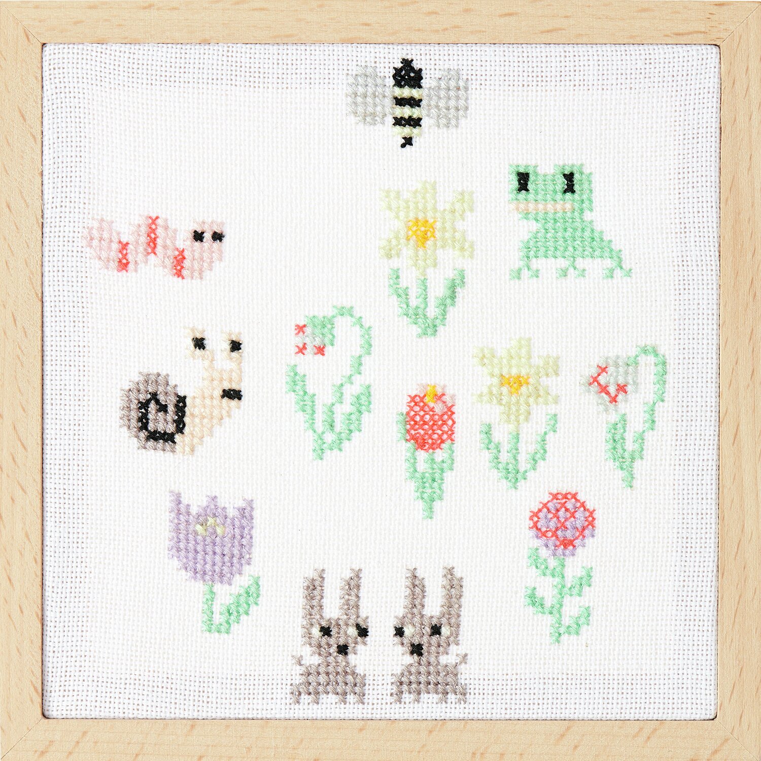 Stickbuch Futschikato 183: Bunte Kreuzstichmotive mit Tieren und Blumen auf weißem Stoff, gerahmt in Holz.