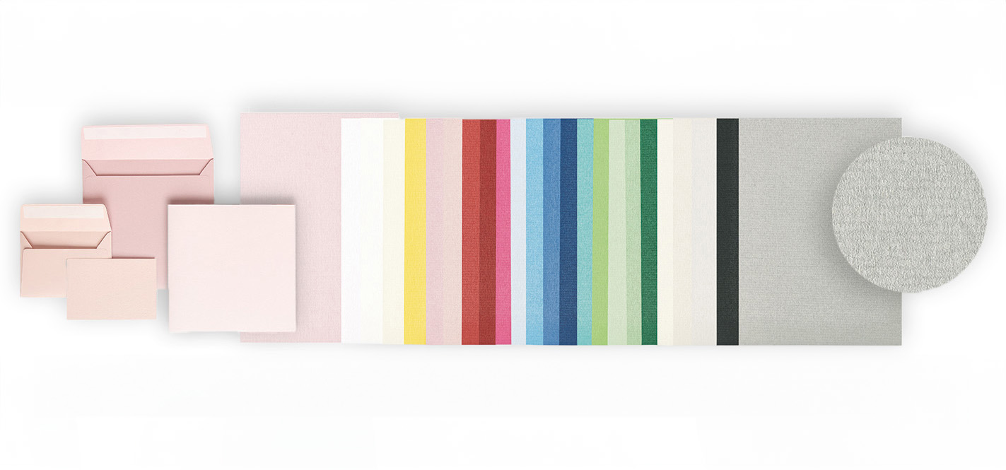 Rosa Umschläge in verschiedenen Größen daneben Karten nach Farben sortiert. Flatlay von Produkten.