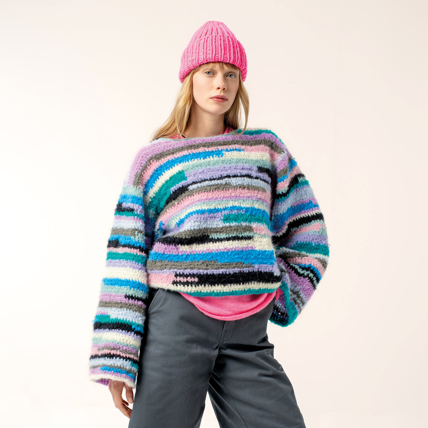 Häkelanleitung Pullover aus Fashion Light Luxury: Bunter, gestreifter Pullover mit pinker Mütze, getragen von einer Frau.