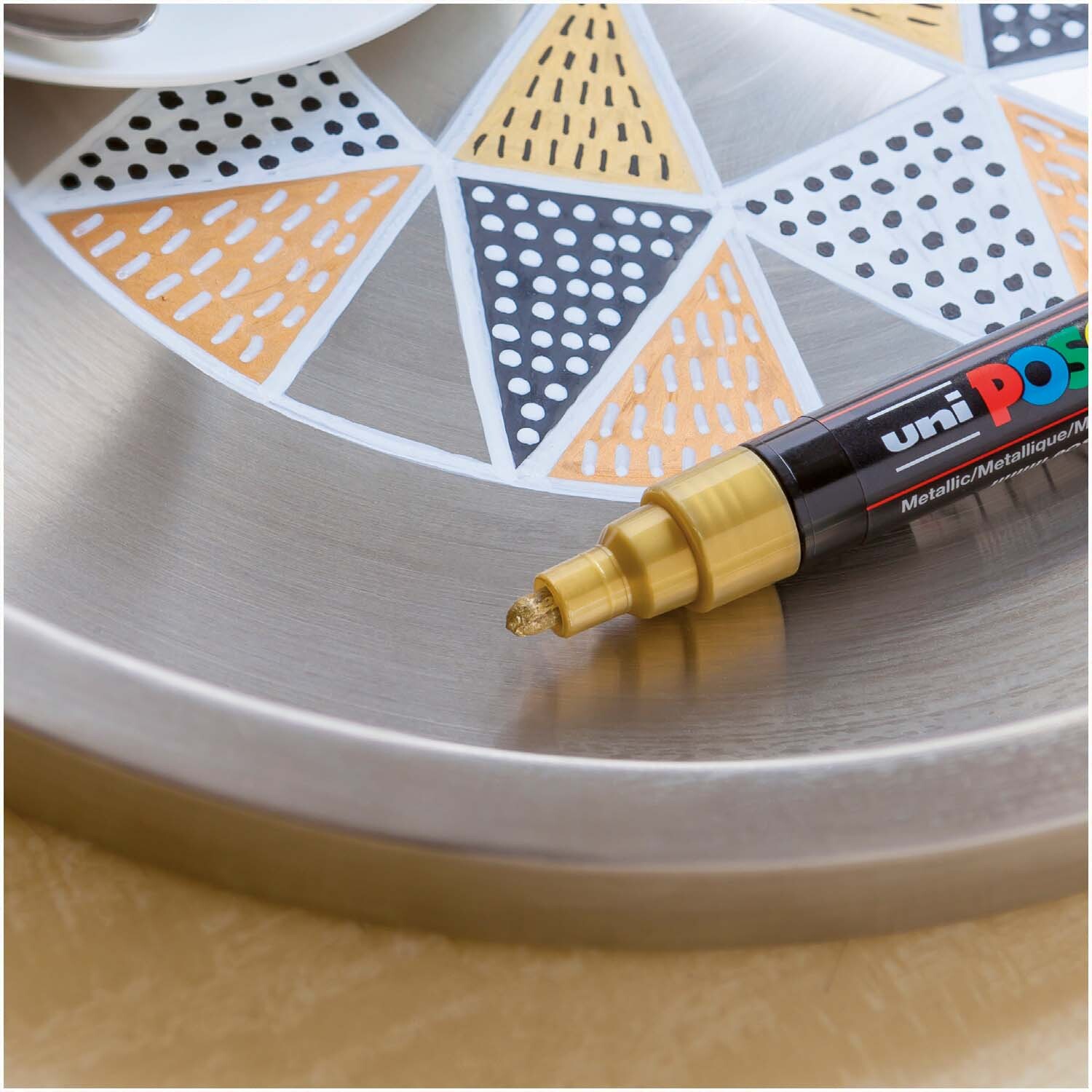 POSCA-Marker PC-3M 0,9-1,3mm in Gold von uni, auf einem dekorativen Tablett mit geometrischem Muster.