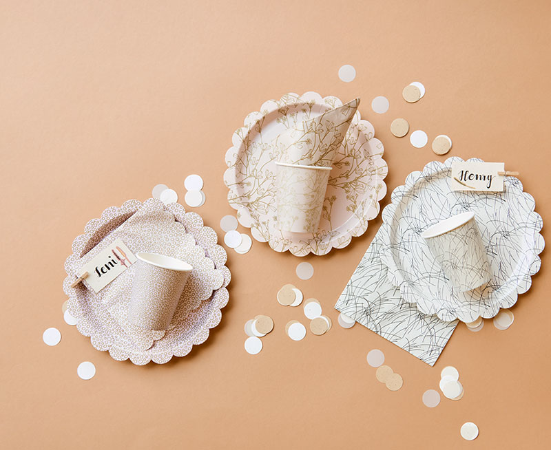 Pappteller, -becher und Servietten in drei unterschiedlichen Motiven, dazu bräunliches Konfetti. Flatlay von Produkten aus der Kollektion In The Meadow.