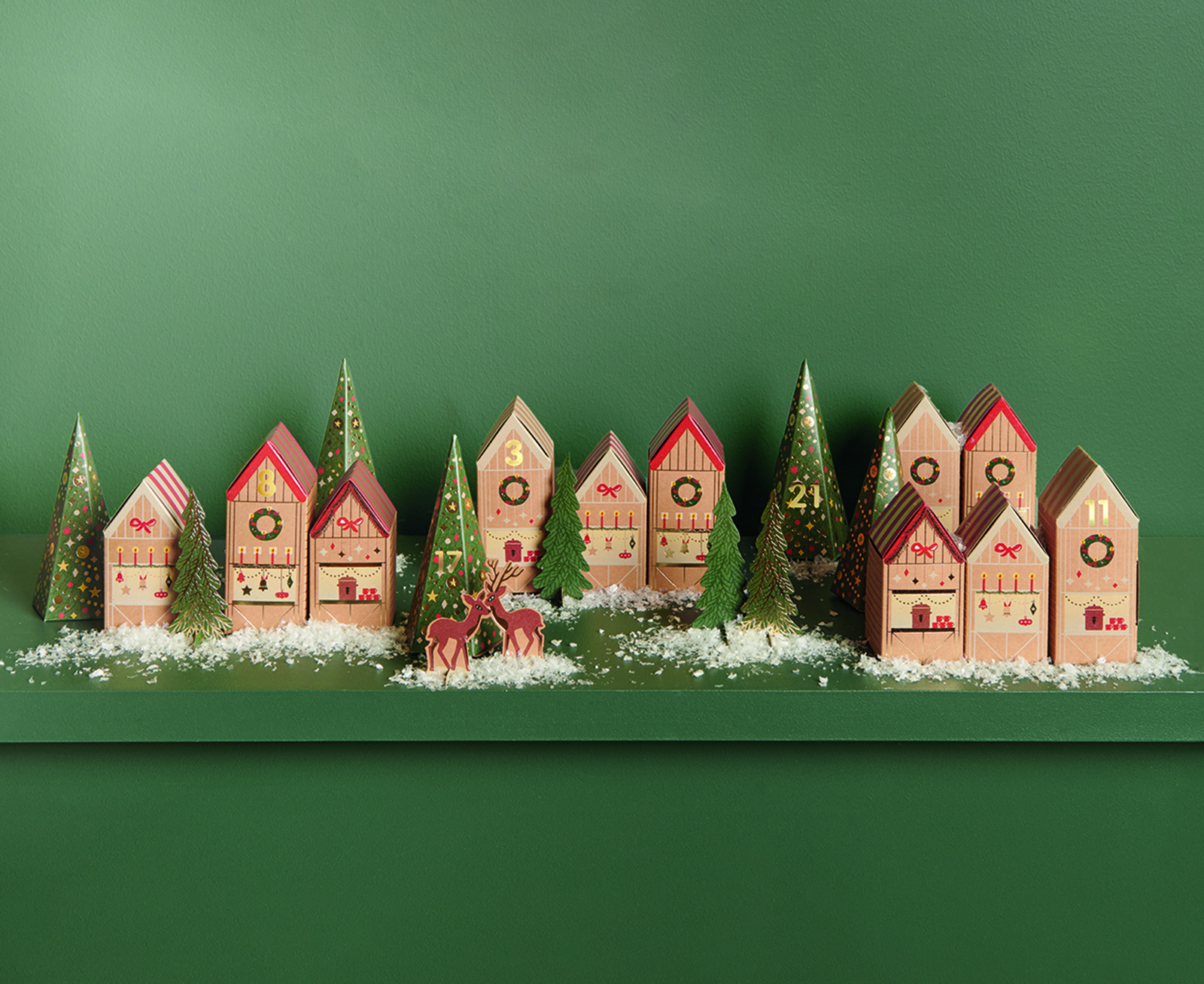 Papphäuser und Papptannen stehen dekoriert vor einem grünen Hintergrund