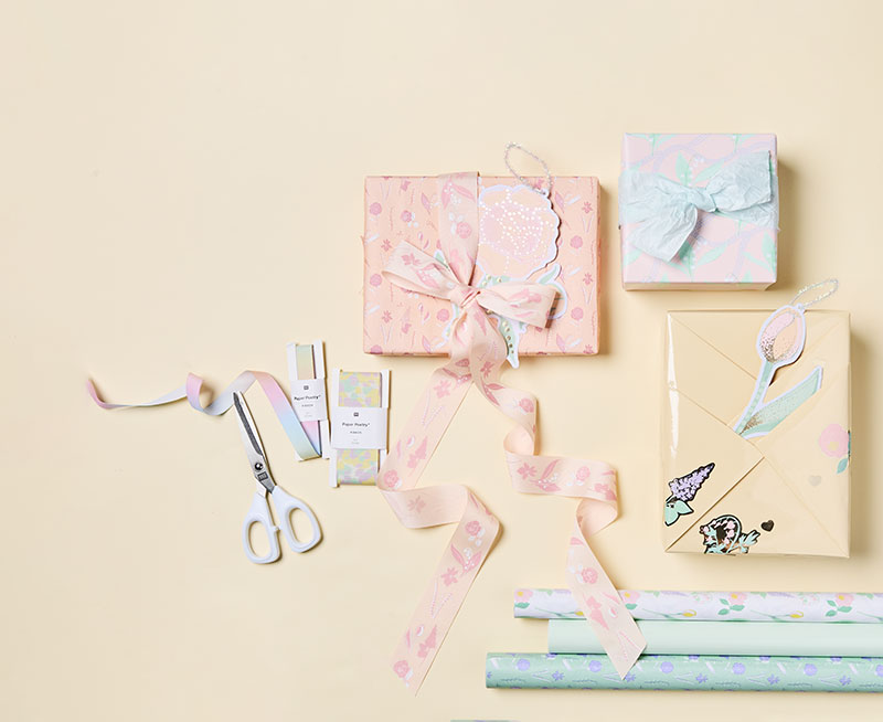 Geschenkpapier, Geschenkbänder und Geschenkanhänger mit floralen Motiven, sowie damit verpackte Geschenke. Flatlay von Produkten der Kollektion The Sky Is The Limit.