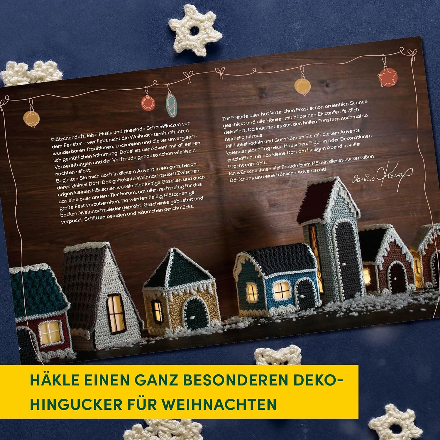 Mein gehäkeltes Weihnachtsdorf - Adventskalenderbuch: Gehäkelte Häuser auf Holzuntergrund, dekoriert mit Lichtern und Schneeflocken.