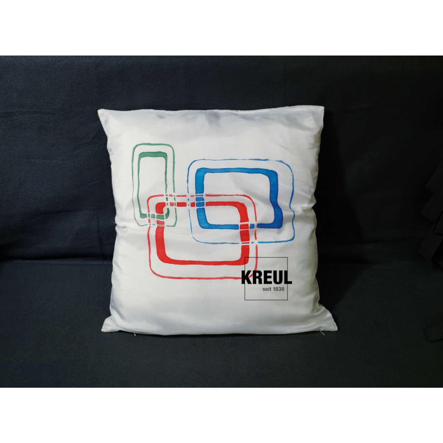 Javana Seidenmalfarben-Set Grundfarben: Weißes Kissen mit buntem, geometrischem Muster und KREUL-Logo.