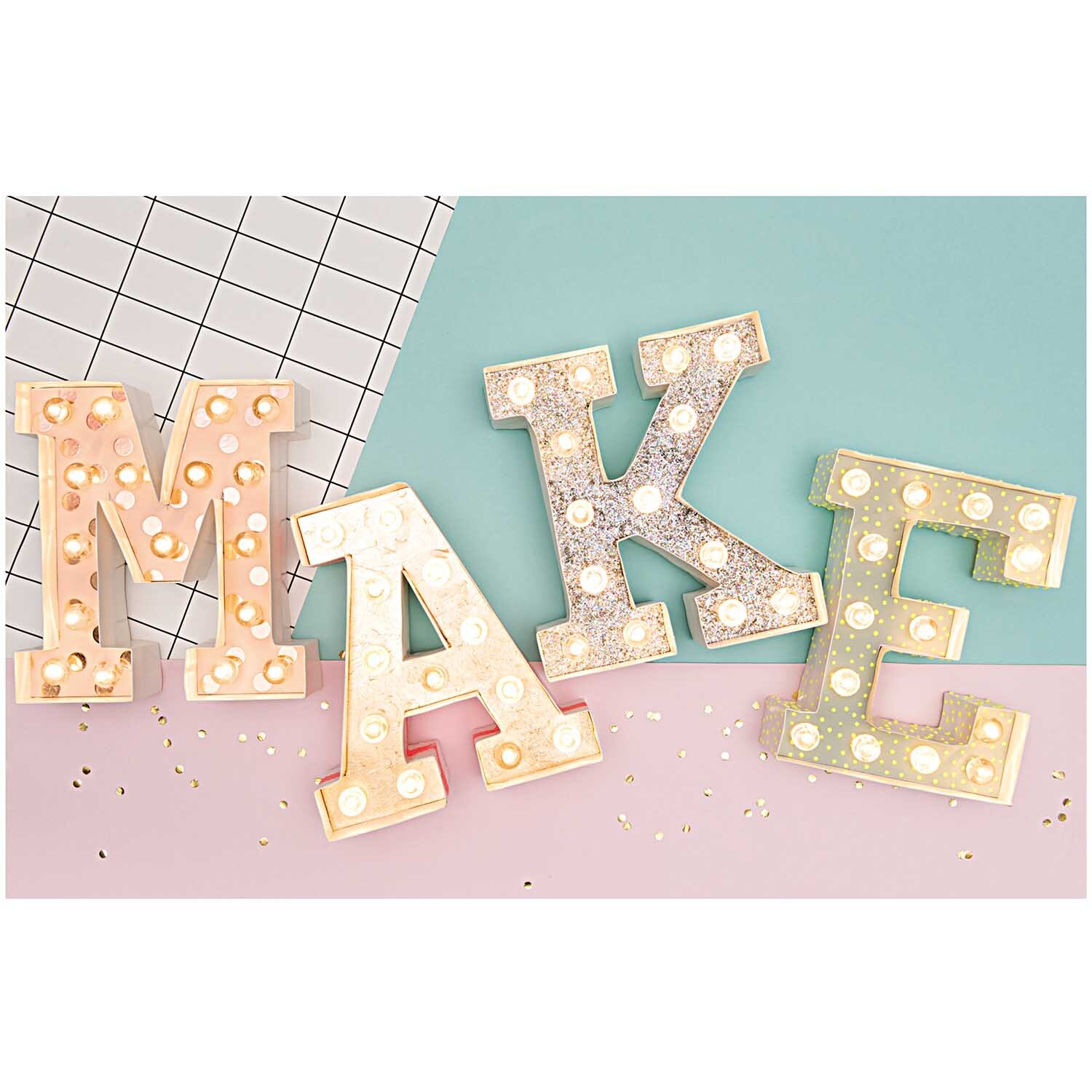 LED Leucht-Buchstaben von Rico Design in Pastellfarben, die das Wort "MAKE" auf einem geometrischen Hintergrund bilden.