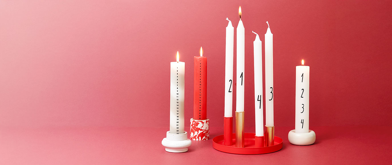Verschiedenen Adventskalender- und Adventskerzen in verschiedenen Kerzenhaltern. Fotosetting roter Hintergrund.