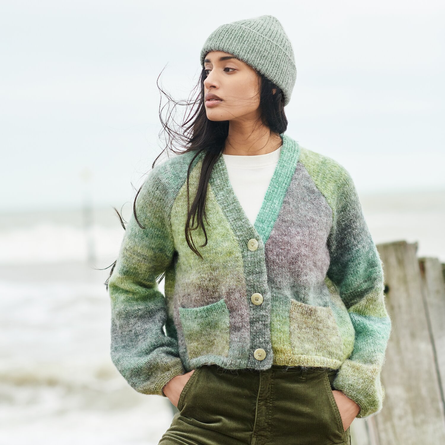 Strickset Jacke Modell 16 aus Lovewool No. 21 von Rico Design Strickset Jacke Modell 16 aus Lovewool No. 21, grüne und graue Töne, am Strand getragen.