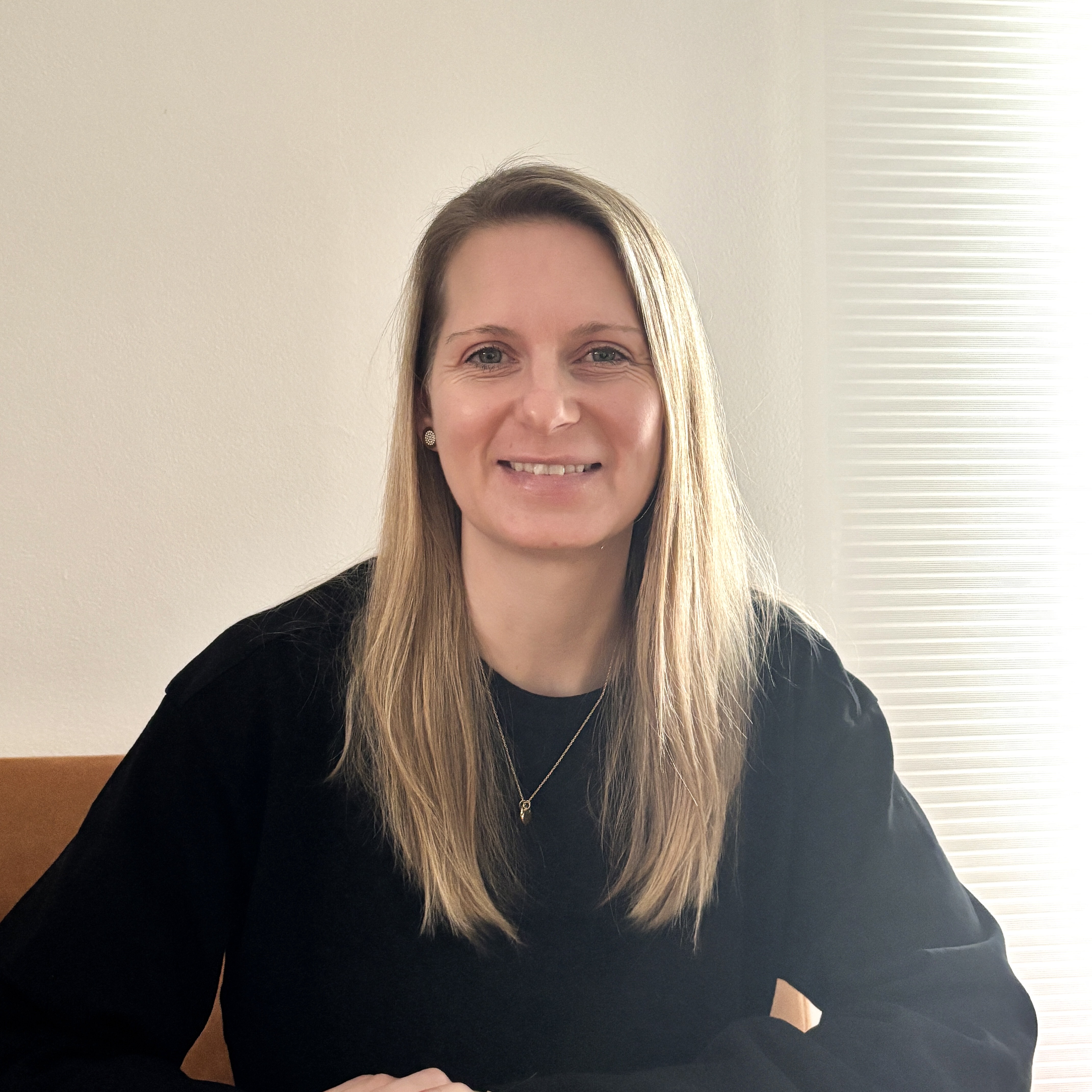 Eine Frau mit langen blonden Haaren und einem schwarzen Pullover lächelt.