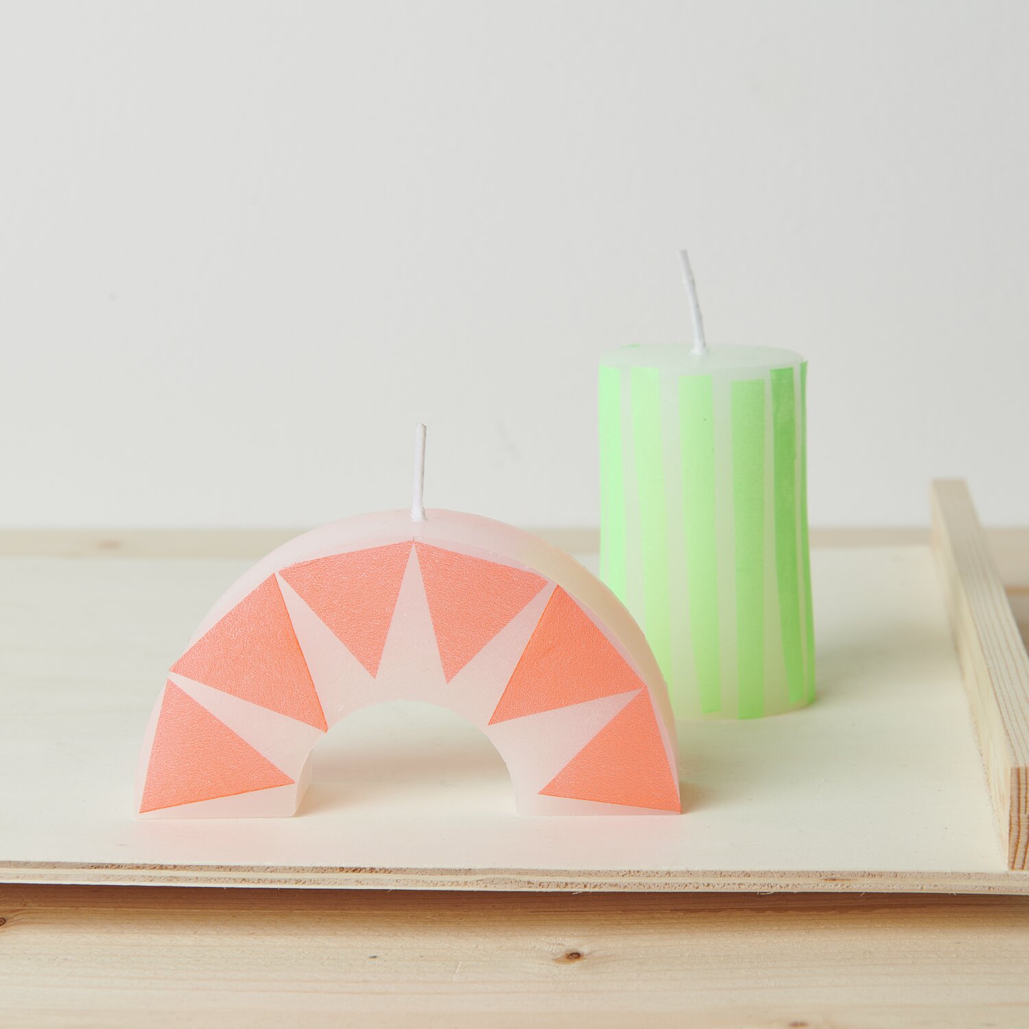 Kerzenwachs Granulat Größe 300g von Rico Design Kerzenwachs Granulat: Zwei dekorative Kerzen, eine in Pastellgrün gestreift, die andere in Halbkreisform mit rosa Dreiecken.
