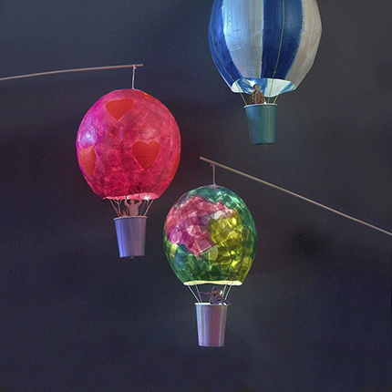 Drei Heißluftballon-Laternen in verschiedenen Farben und Mustern. Fotosetting schwarze Wand.