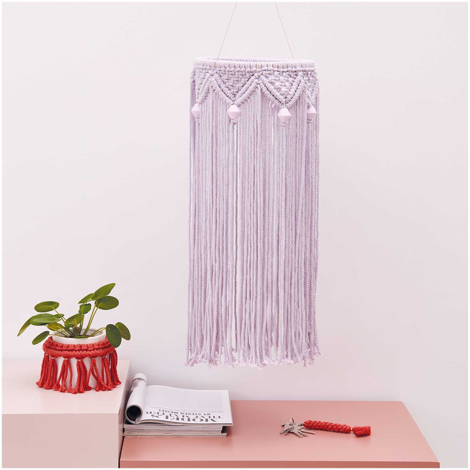 Creative Cotton Cord Makramee-Garn: Wandbehang aus lavendelfarbenem Garn, dekorativ und handgefertigt, neben Pflanzen und Notizbuch.