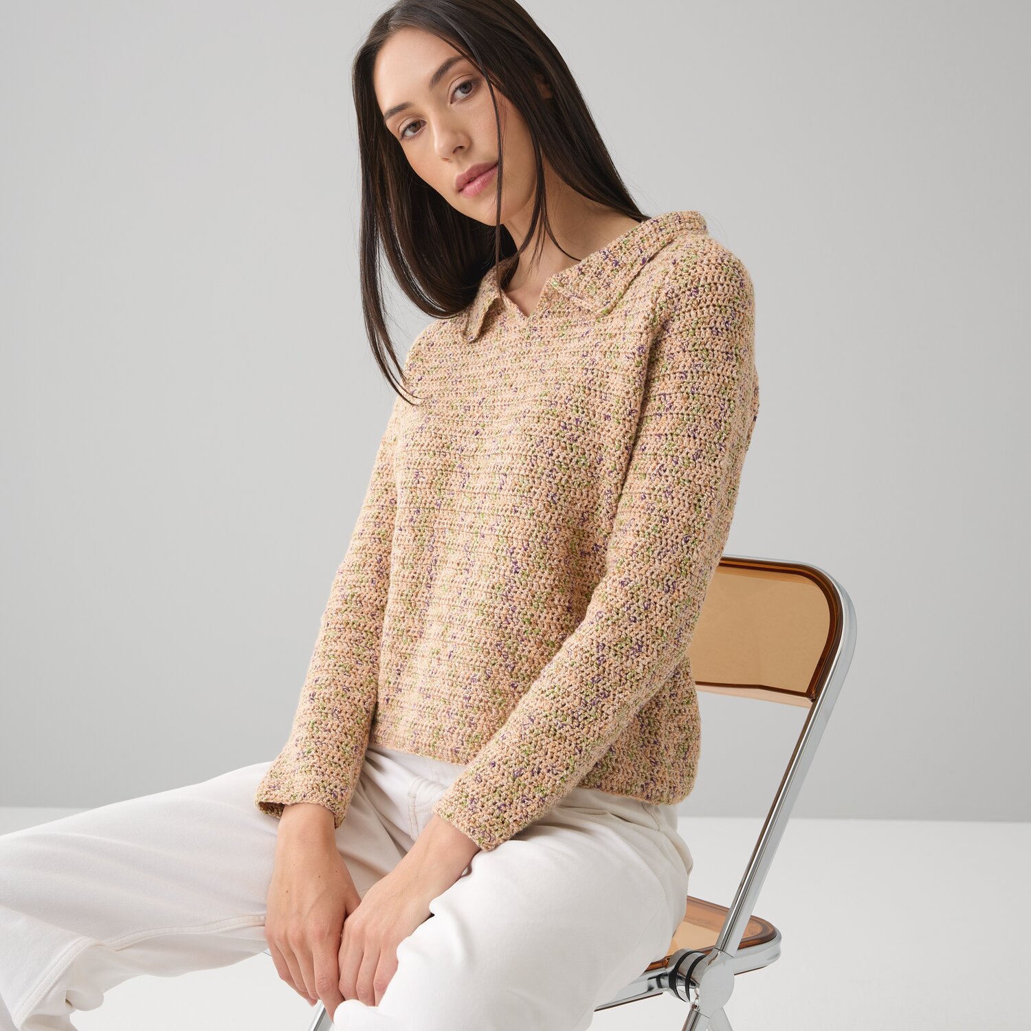 Häkelset Pullover Modell 15: Beiger Strickpullover, getragen von Frau auf Stuhl, weiße Hose.