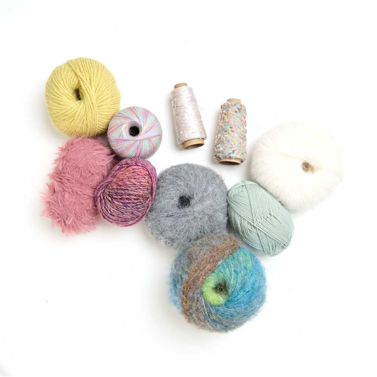 Mehrere kleine Garnknäuel und Wollproben in Gelb, Rosa, Grau, Blau, Grün und Weiß