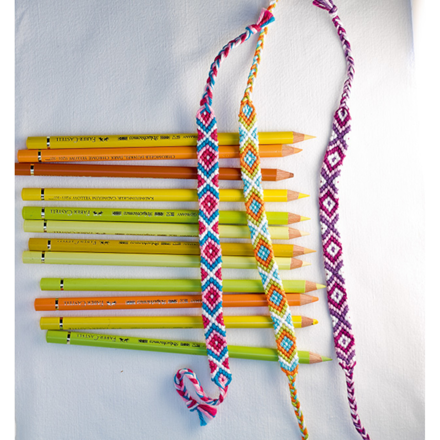 Freundschaftsbänder - Die beliebtesten Muster: Bunte Bänder neben gelben und orangen Stiften auf weißem Hintergrund.