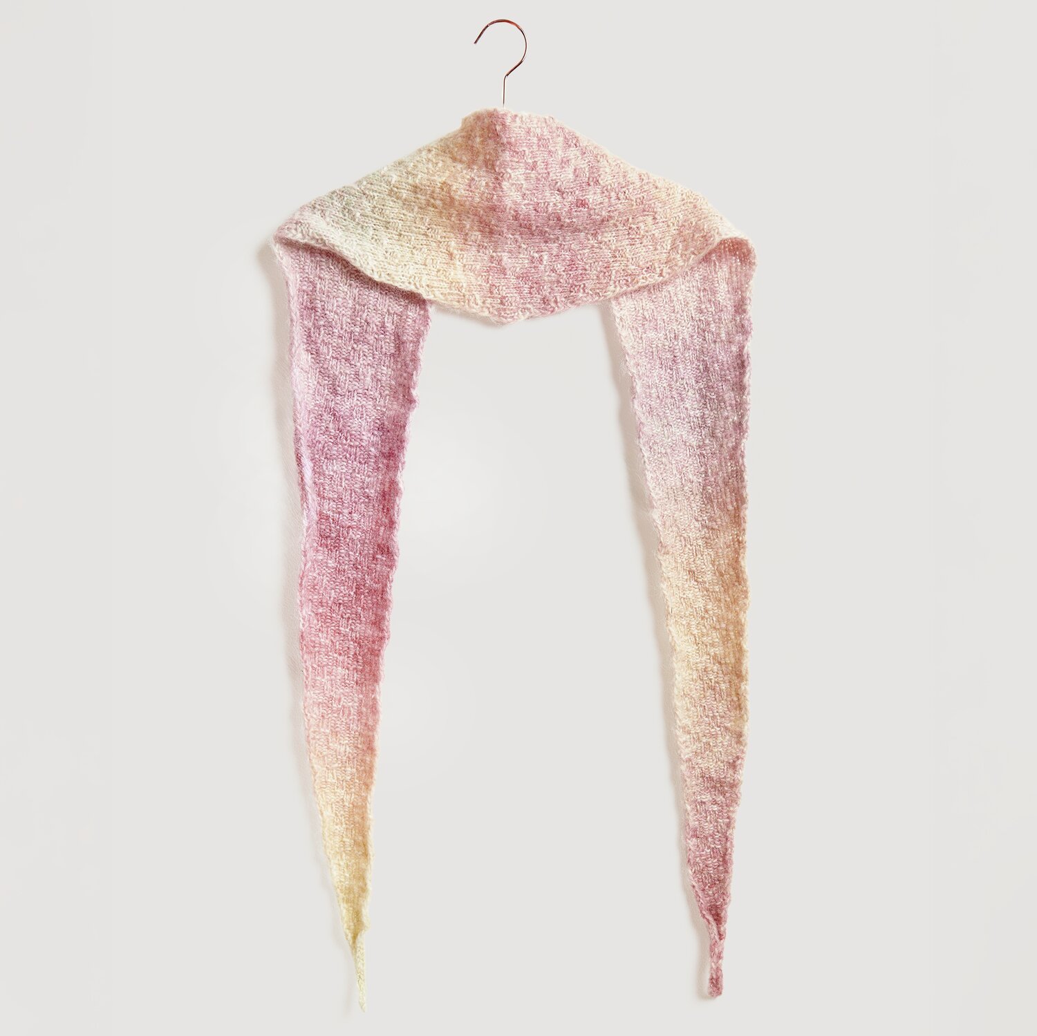 Die Neue Masche No. 13 Herbst von idee. Creativmarkt Strickset Dreieckstuch Modell 06 aus Die Neue Masche No. 13 in sanften Erdtönen, aufgehängt an einem Haken.
