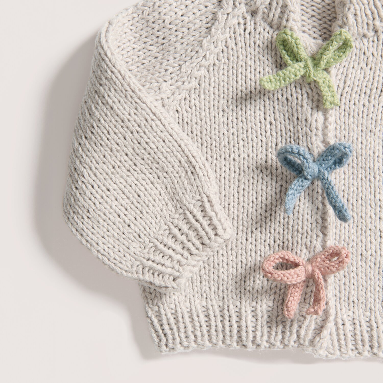 Rico Baby 043 Strickjacke aus Bio-Baumwolle mit Schleifen in Salbei, Taubenblau und Blush.