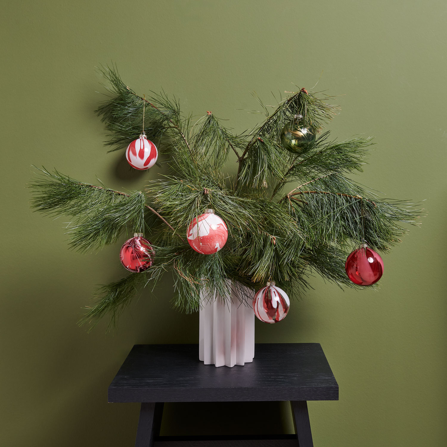 Kieferzweige dekorativ in einer Vase und mit unterschiedlichen Weihnachtsbaumkugeln geschmückt. Fotosetting grüner Hintergrund.