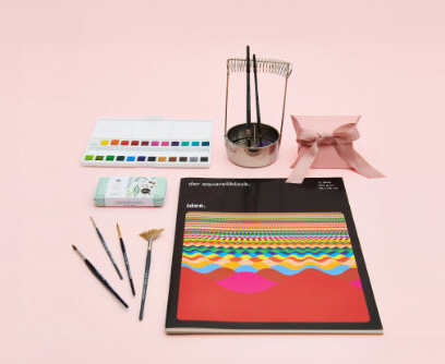 Verschiedene Materialien zum Aquarell malen. Ein Aquarellblock mit Aquarellfarbkasten, Pinseln und Pinselwascher. Fotosetting rosa Hintergrund.