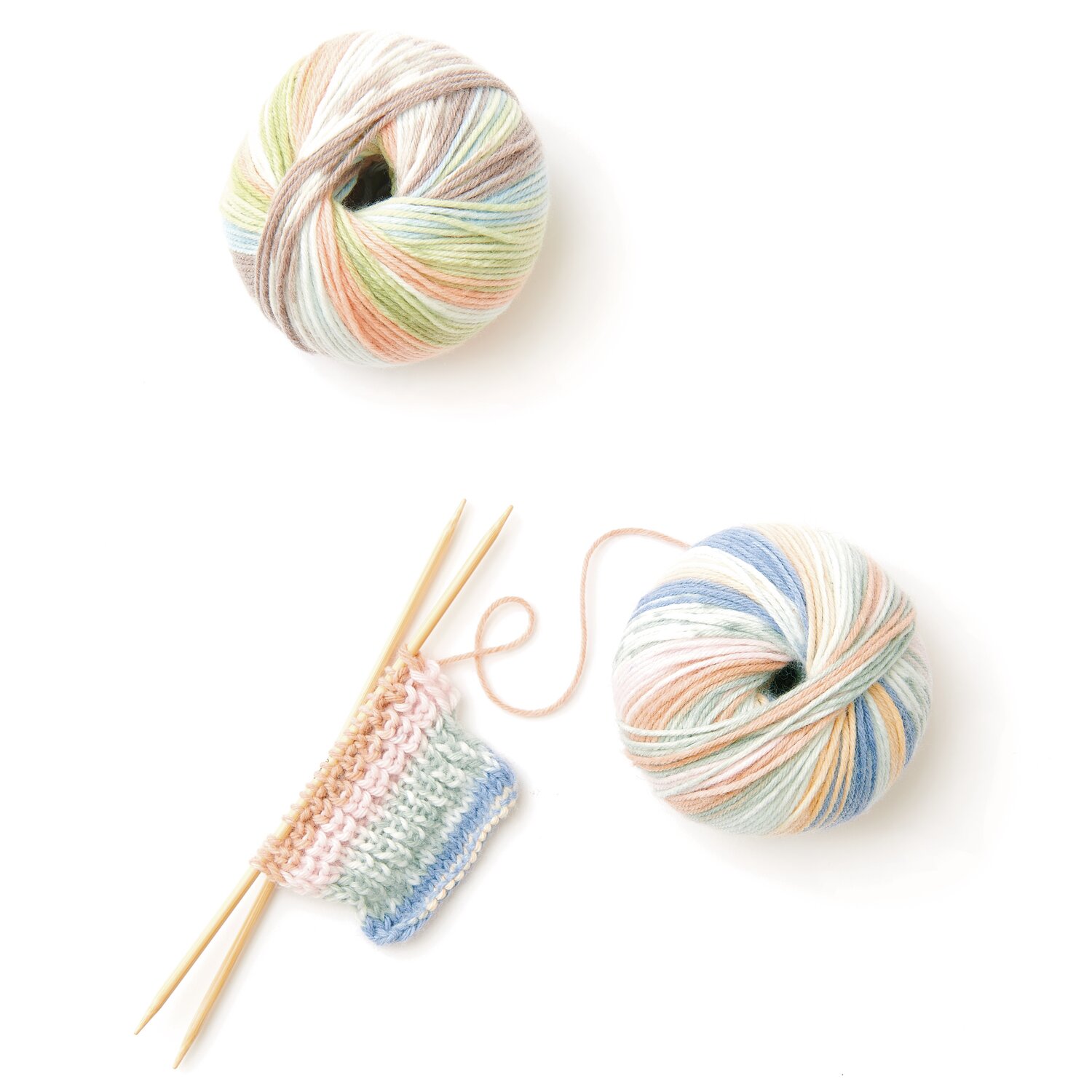 Rico Baby 042 Wolle in sanften Pastelltönen, gestricktes Muster und Stricknadeln auf weißem Hintergrund.
