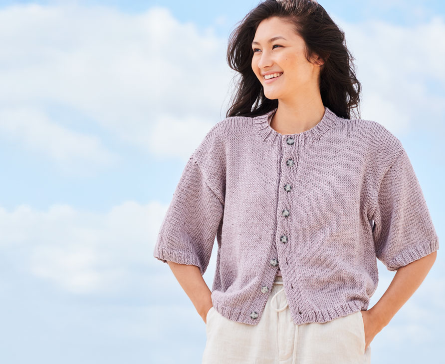 Frau mit fliederfarbener Strickjacke steht vor Wolken