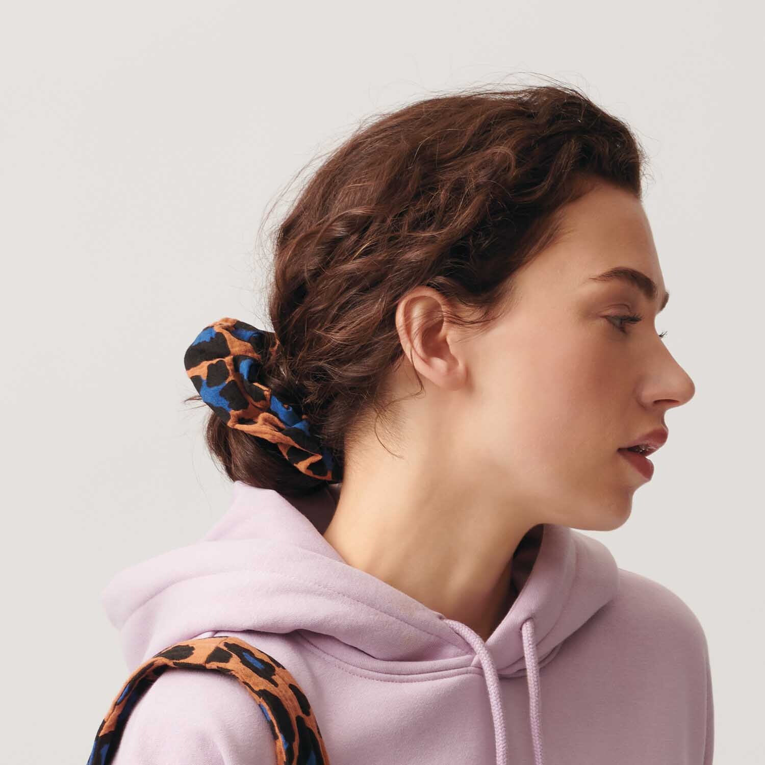 Nähanleitung für Scrunchies aus Stoff: Frau mit lila Hoodie trägt Scrunchie mit Leopardenmuster im Haar.