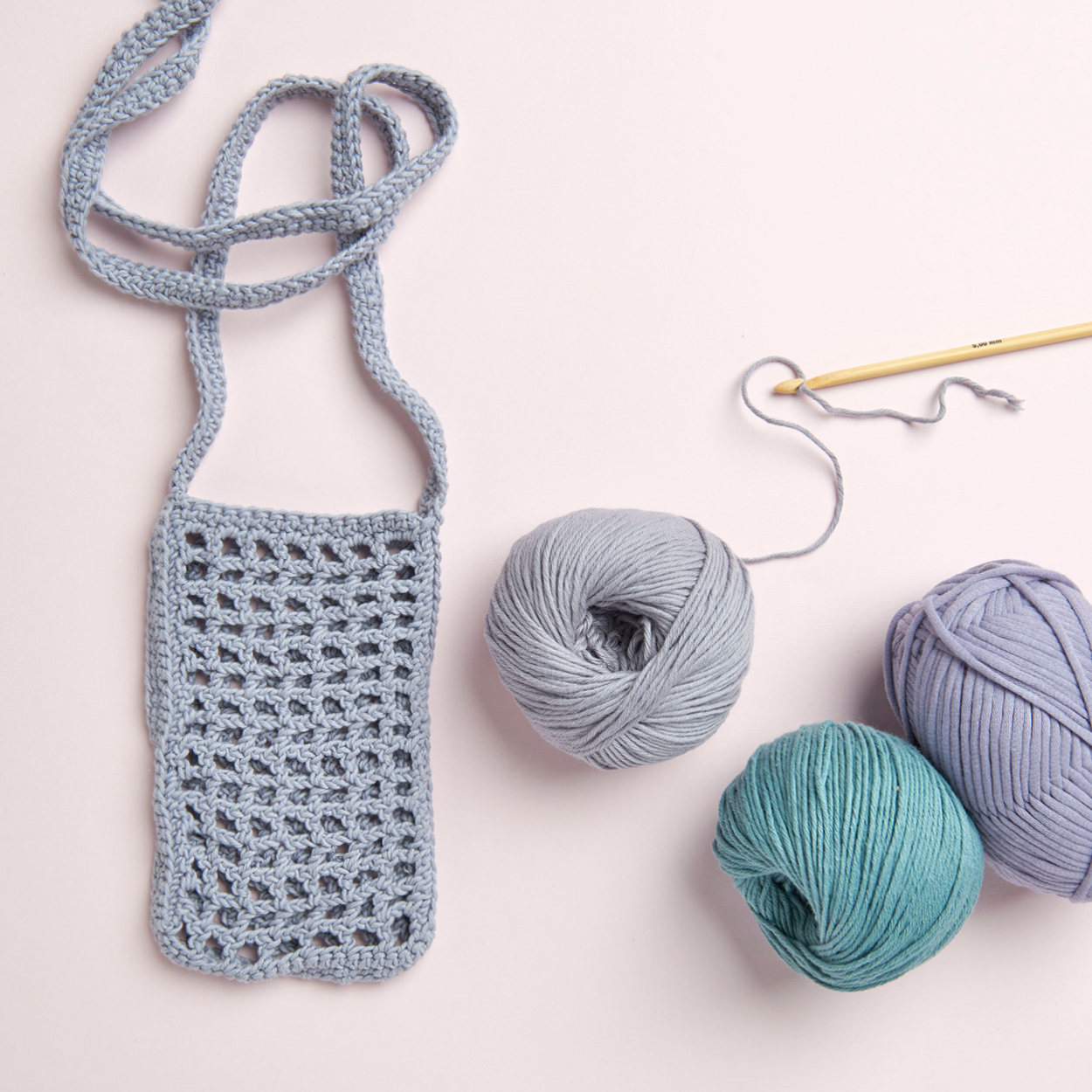 Eine kleine gehäkelte Netztasche aus blauem Garn mit Häkelgarnen und Nadel. Flatlay von Produkten.