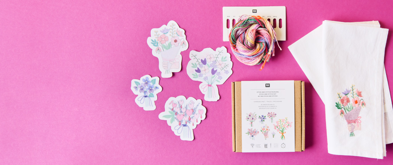 Ein Stick and Stitch Set aus der Kollektion The Sky Is The Limit mit floralen Motiven, daneben ein bereits bestickter Stoff. Flatlay von Produkten.
