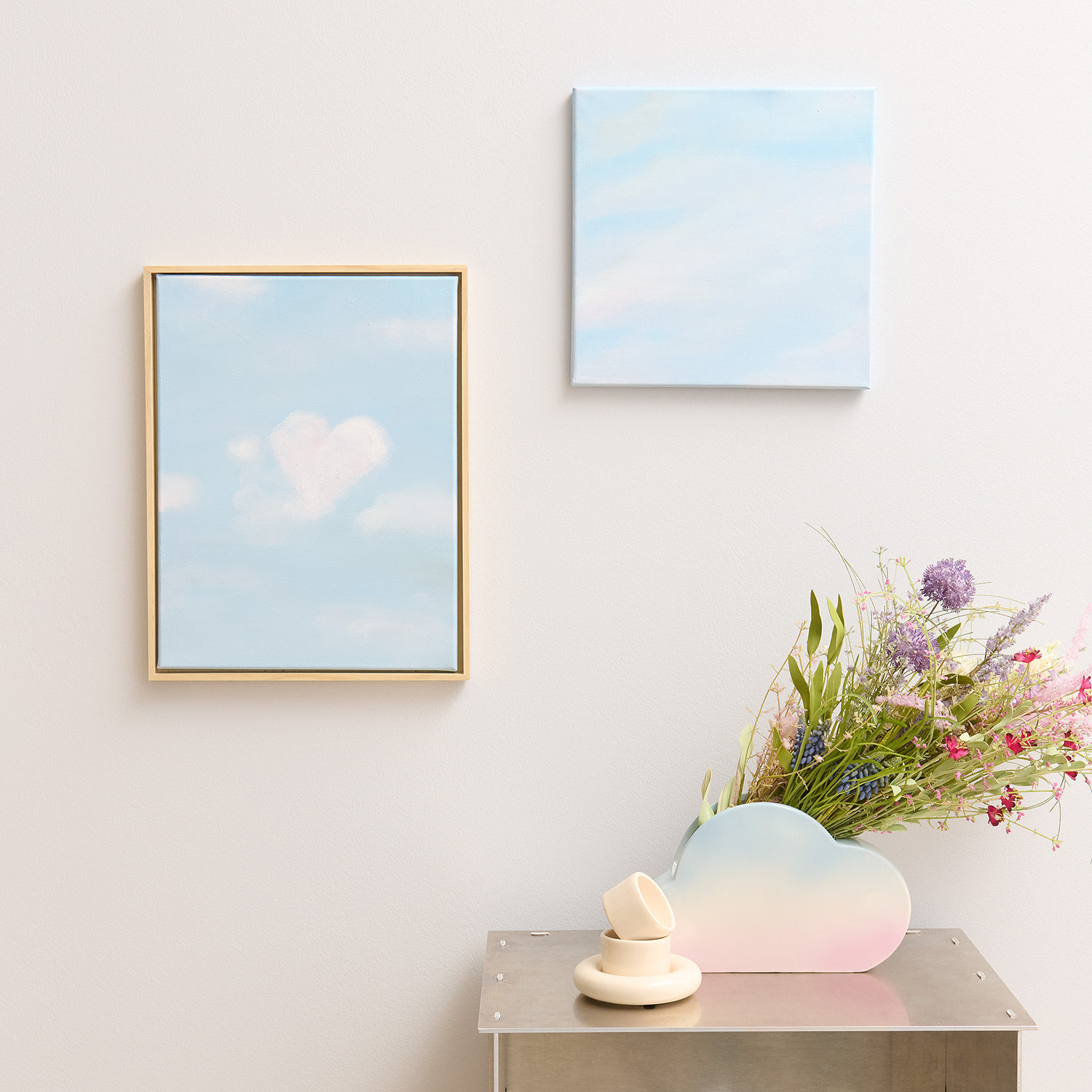 Anleitung Wolkenbild mit Acrylfarbe malen: Zwei blaue Gemälde mit Wolkenmotiv an weißer Wand.