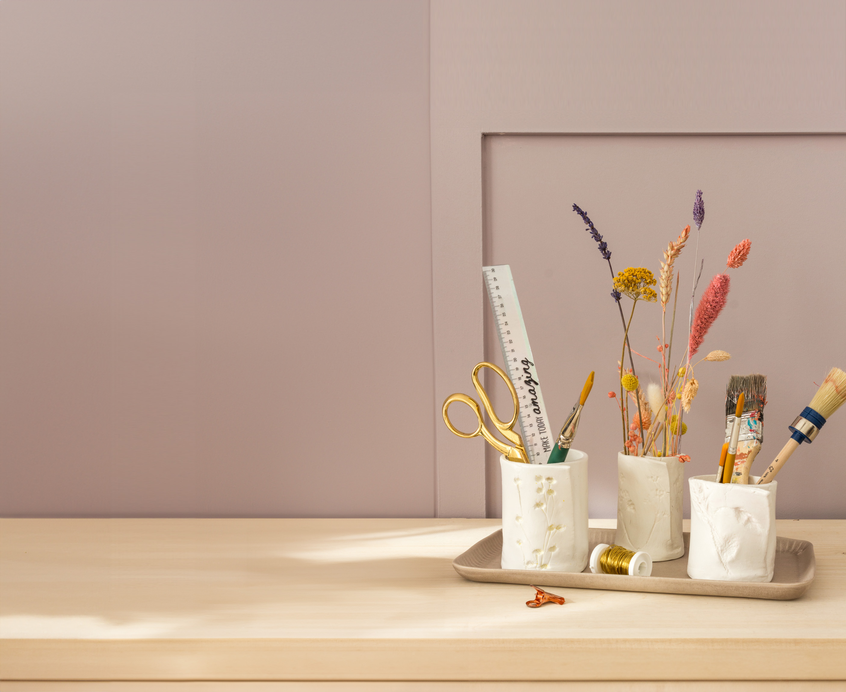 Drei Stiftehalter aus Modelliermasse mit Schreib- und malmaterial, sowie Trockenblumen befüllt. Fotosetting Holzregal und braune Wand.