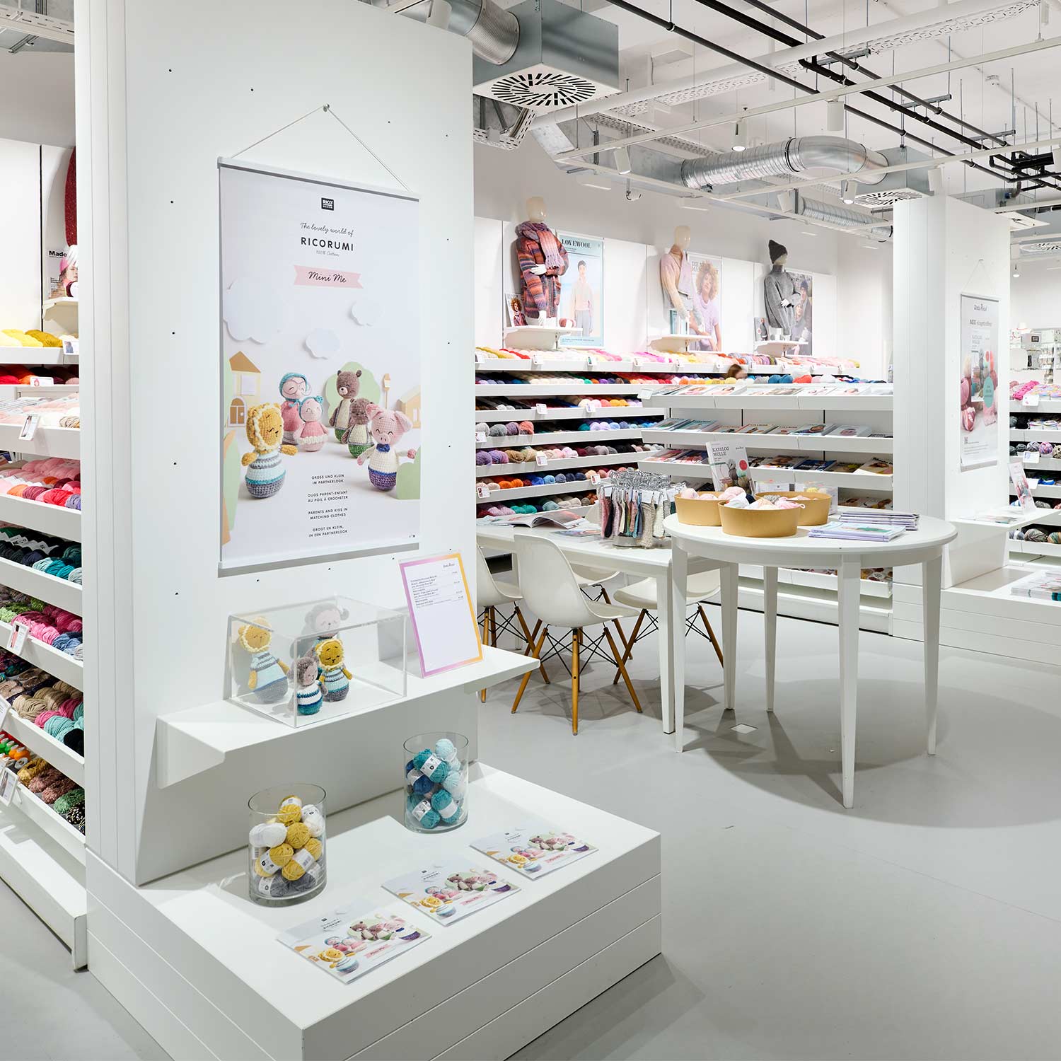 Die Wolle Rödel Abteilung in einer idee. Creativmarkt Filiale. Regale mit verschiedenen Garnen und ein Tisch mit Stühlen in der Mitte.