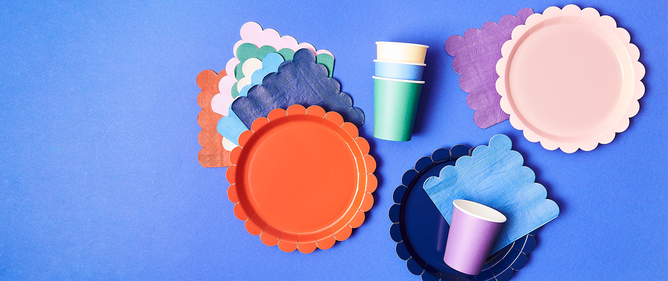 Zusammenpassende Papierteller, -becher und Servietten in verschiedenen Farben. Flatlay von Produkten.