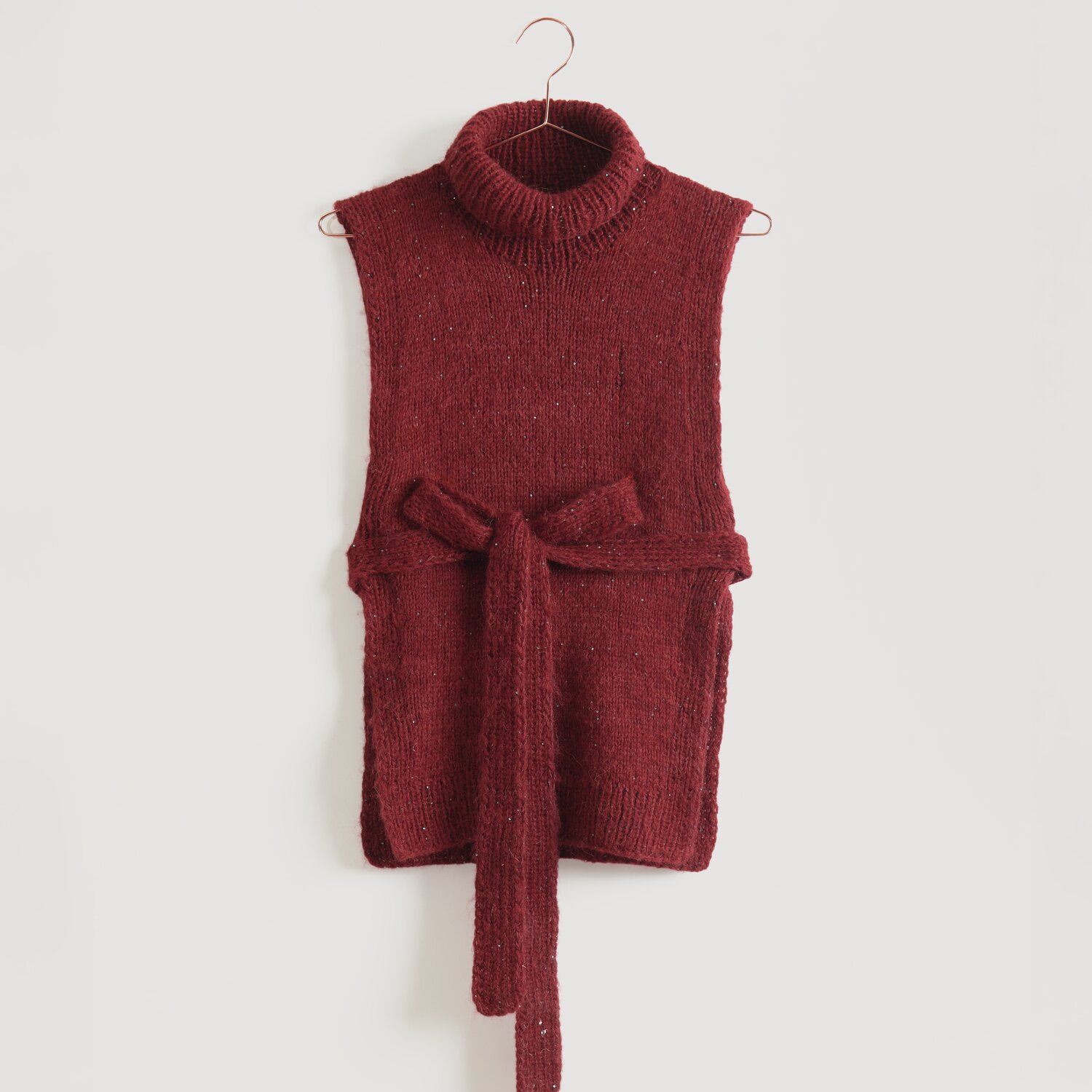 Lovewool No. 21 Herbst-Winter Sprachauswahl deutsch von Rico Design Ärmelloser, roter Strickpullover mit Rollkragen und Bindegürtel, aufgehängt an einem Kleiderbügel. Marke: Modell Legeware. Perfekt für stilvolle, gemütliche Outfits.