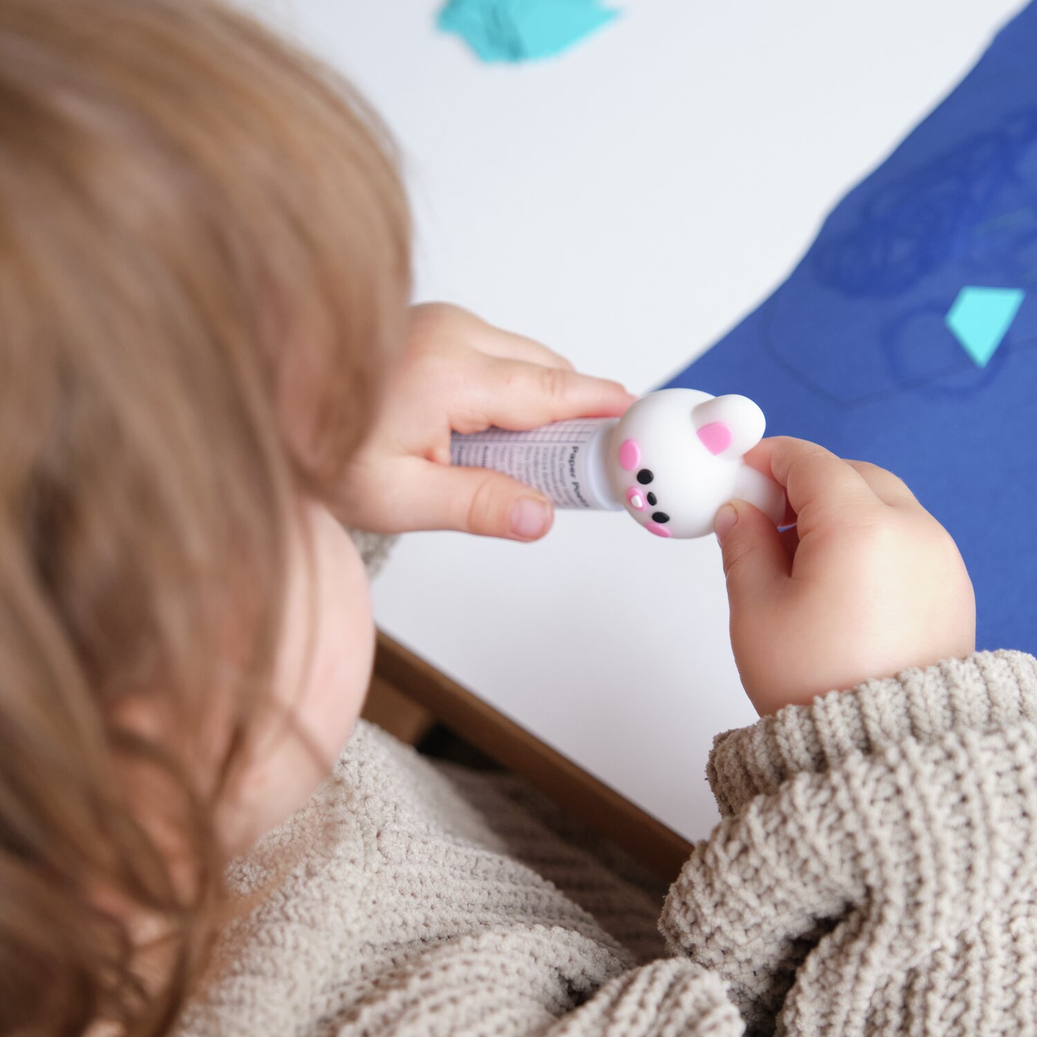 Paper Poetry Klebestift Hase Weiß in Kinderhand, ideal für Bastelarbeiten mit blauen Papieren.
