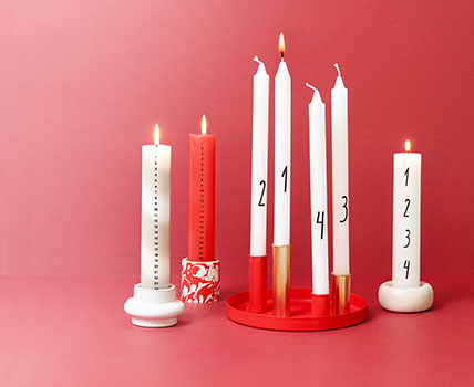 Verschiedenen Adventskalender- und Adventskerzen in verschiedenen Kerzenhaltern. Fotosetting roter Hintergrund.