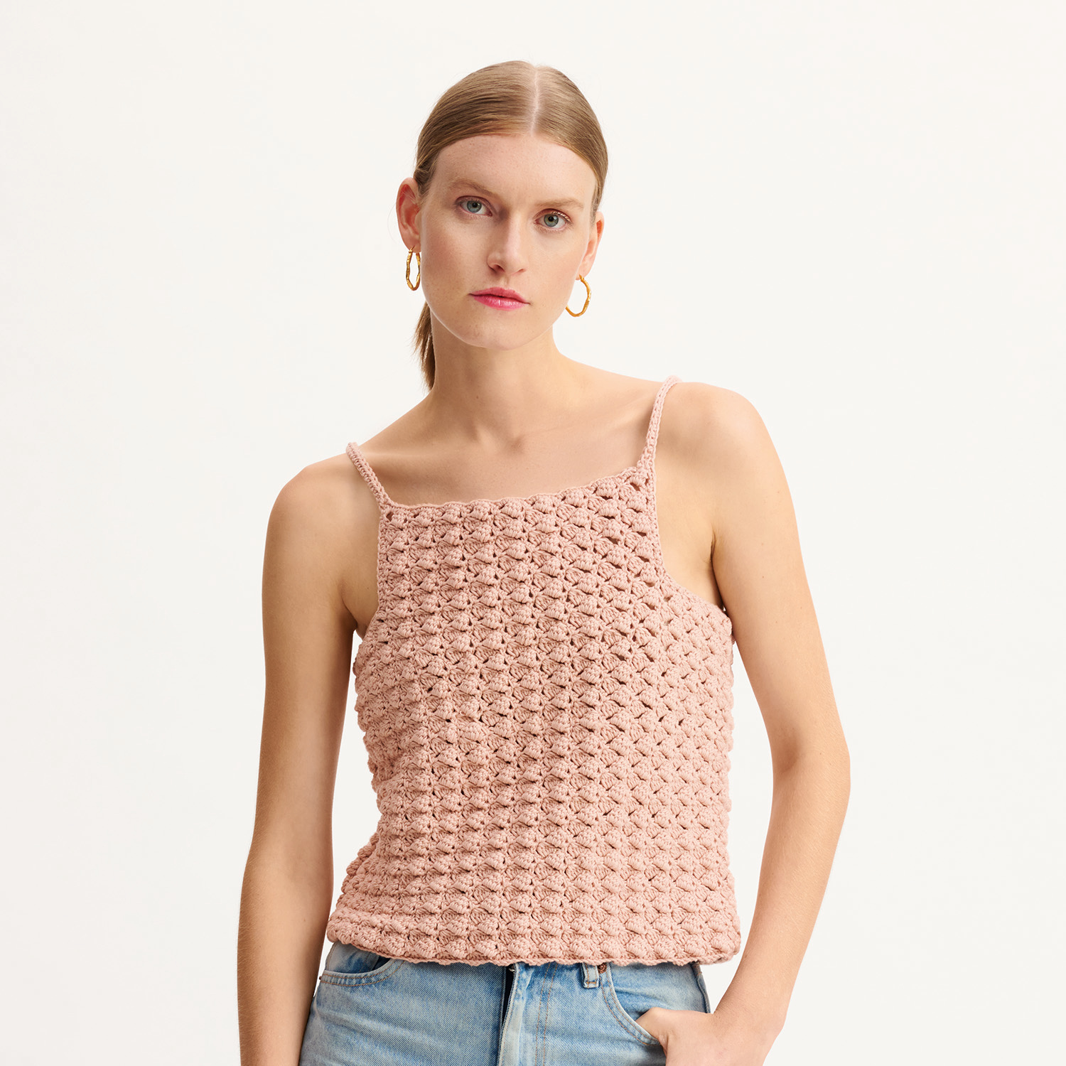 Ärmelloses, gehäkeltes Top in Rosa, getragen von einer Frau mit blonden Haaren und blauen Jeans. Ideal für sommerliche Outfits.