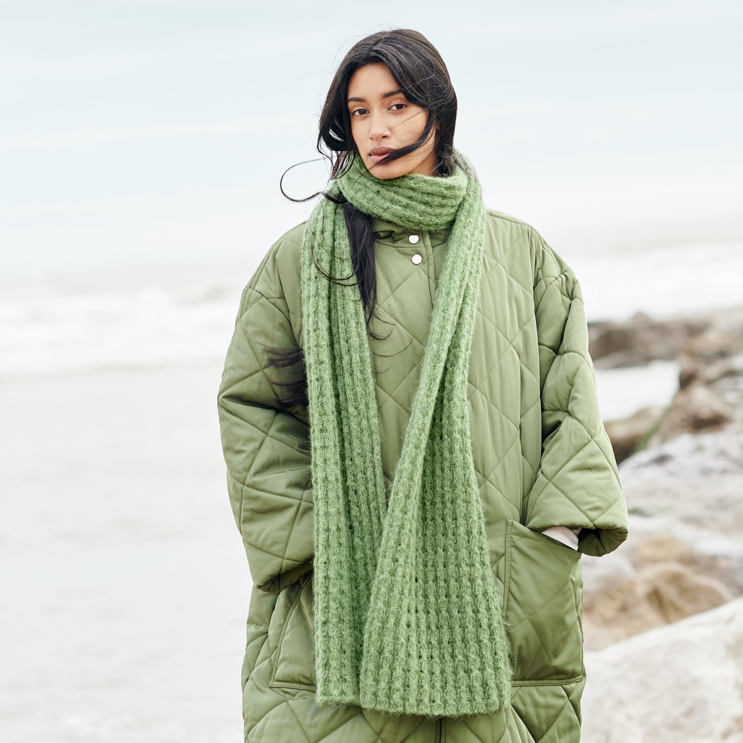 Strickset Schal Modell 07 aus Lovewool No. 21 von Rico Design Strickset Schal Modell 07 aus Lovewool No. 21: Frau am Strand mit grünem Schal und Mantel.