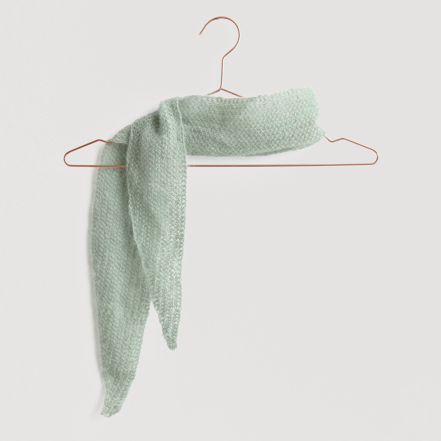 Lovewool No. 21 Herbst-Winter Sprachauswahl deutsch von Rico Design Ein zartgrüner Schal aus weichem Stoff hängt elegant auf einem kupferfarbenen Kleiderbügel. Der Schal ist Teil der Kollektion "Modell Legeware" und bietet stilvolle Wärme für jede Gelegenheit.
