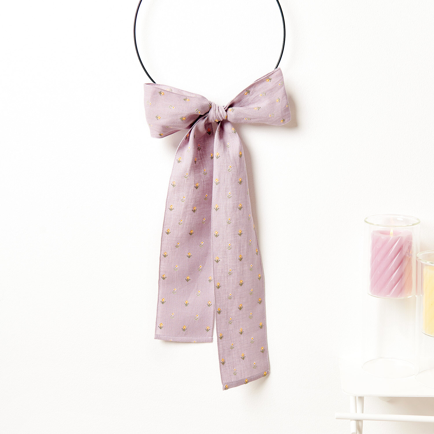 Stickanleitung Dekoschleife mit Blümchen: Lila Schleife mit goldenen Punkten an schwarzem Ring, dekorativ und elegant.