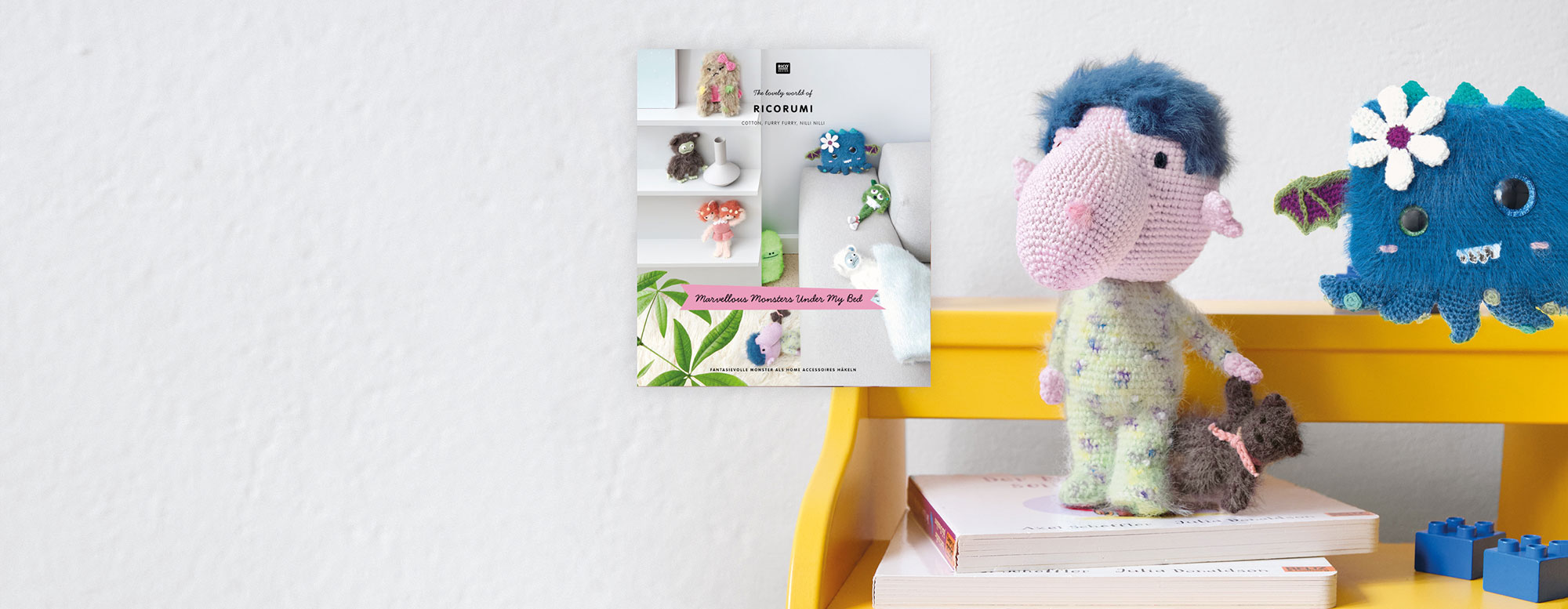 2 gehäkelte Ricorumi Monster stehen auf einer Bank, daneben Anleitungsheft