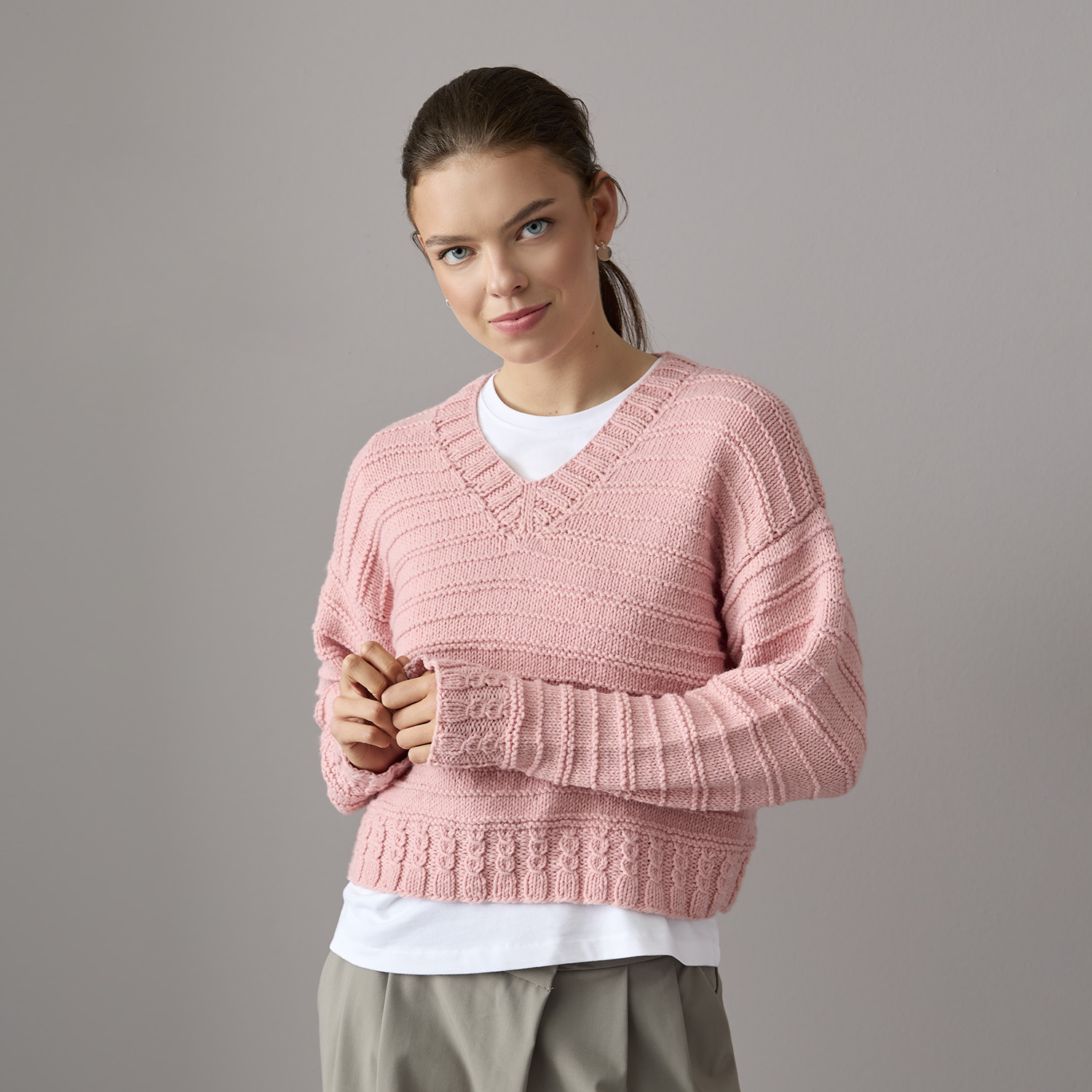 Strickanleitung Pullover aus Essentials Vegan Cashmere aran Strickanleitung Pullover aus Essentials Vegan Cashmere aran: Rosa V-Pullover, lässig gestylt über weißem Shirt, ideal für kühle Tage.