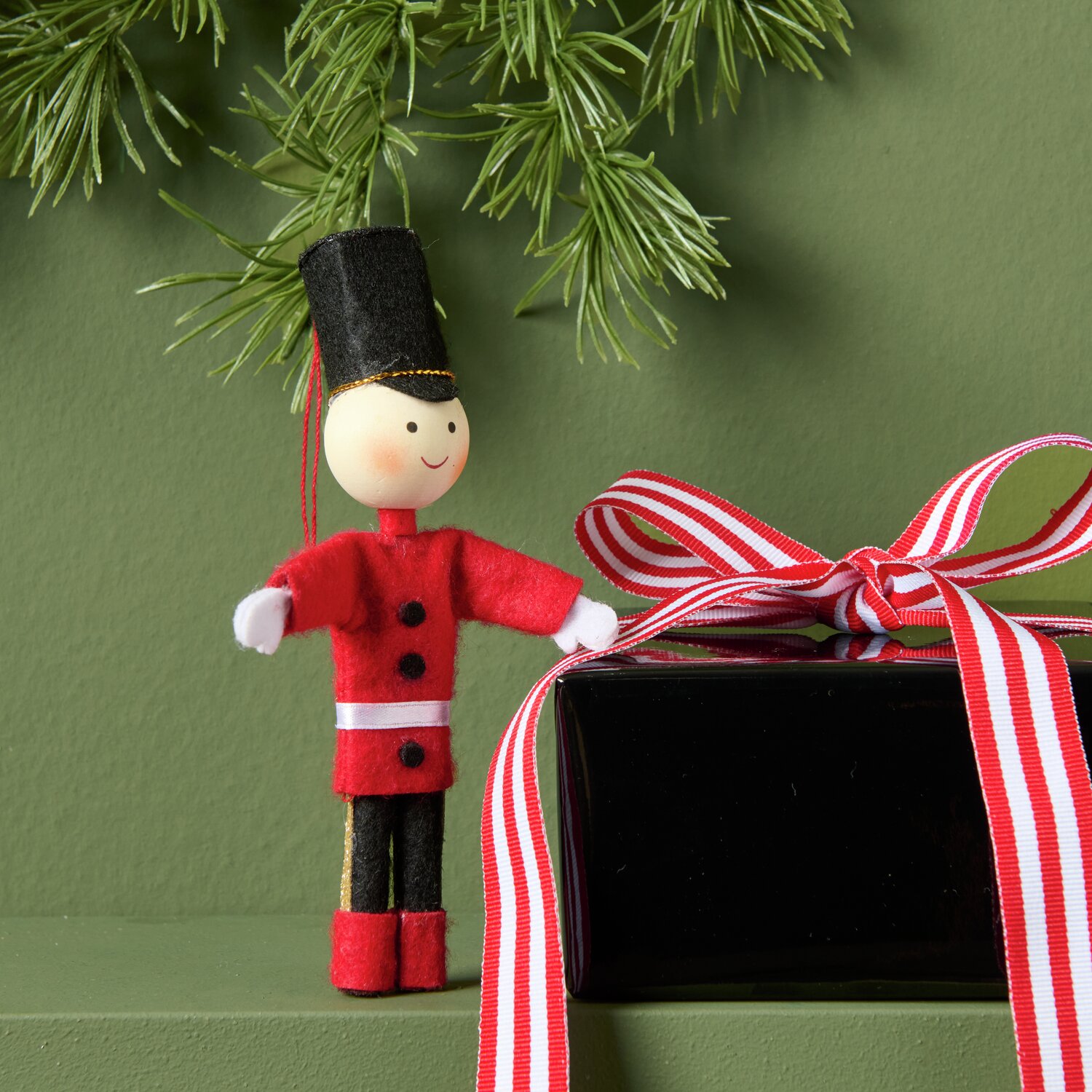 Aufhänger Filz-Soldat Rot/Schwarz: Niedliche Dekofigur neben Geschenk mit rotem Band, ideal für festliche Anlässe.