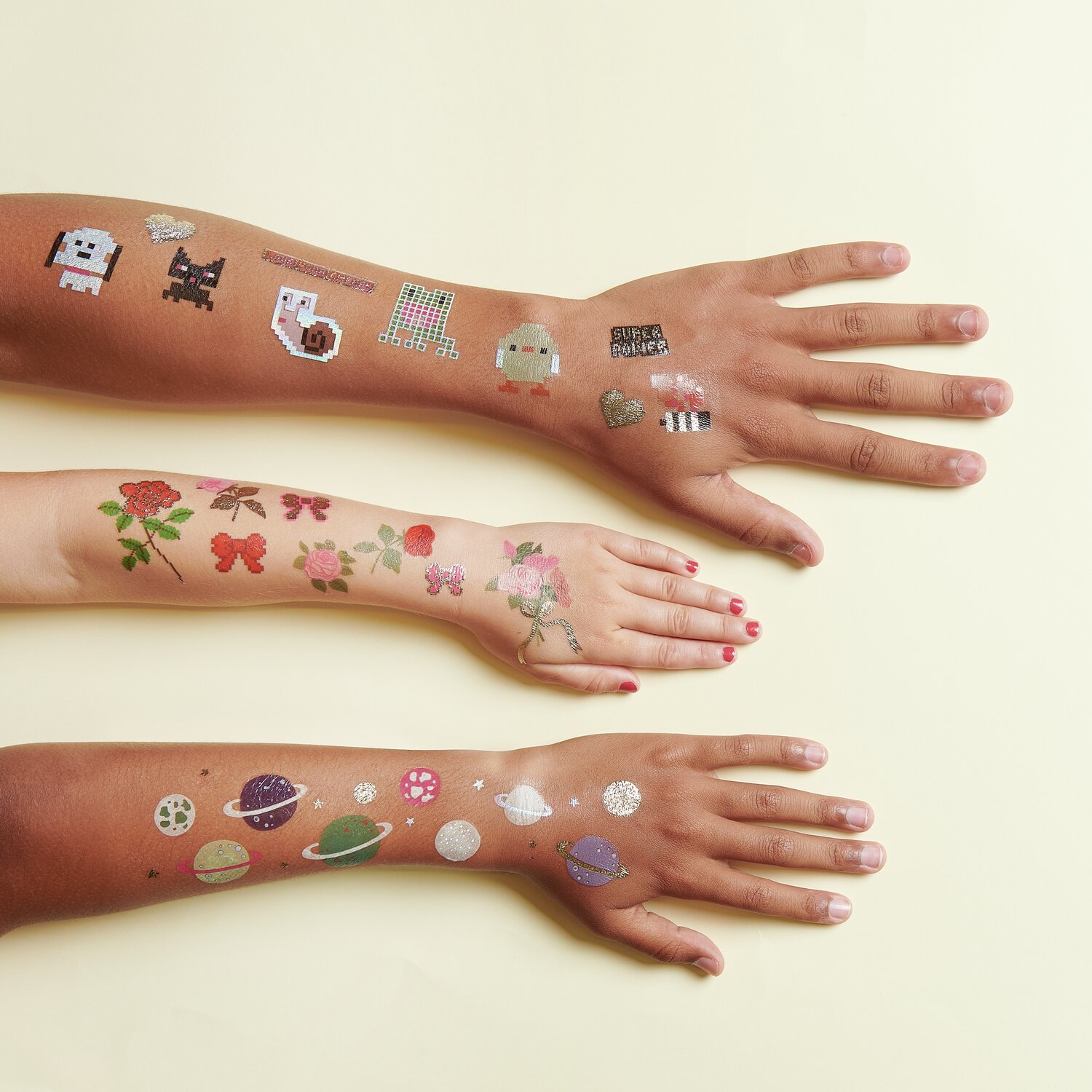 Tattoos Pixel Rosen: Drei Arme mit bunten temporären Tattoos von Tieren, Blumen und Planeten.