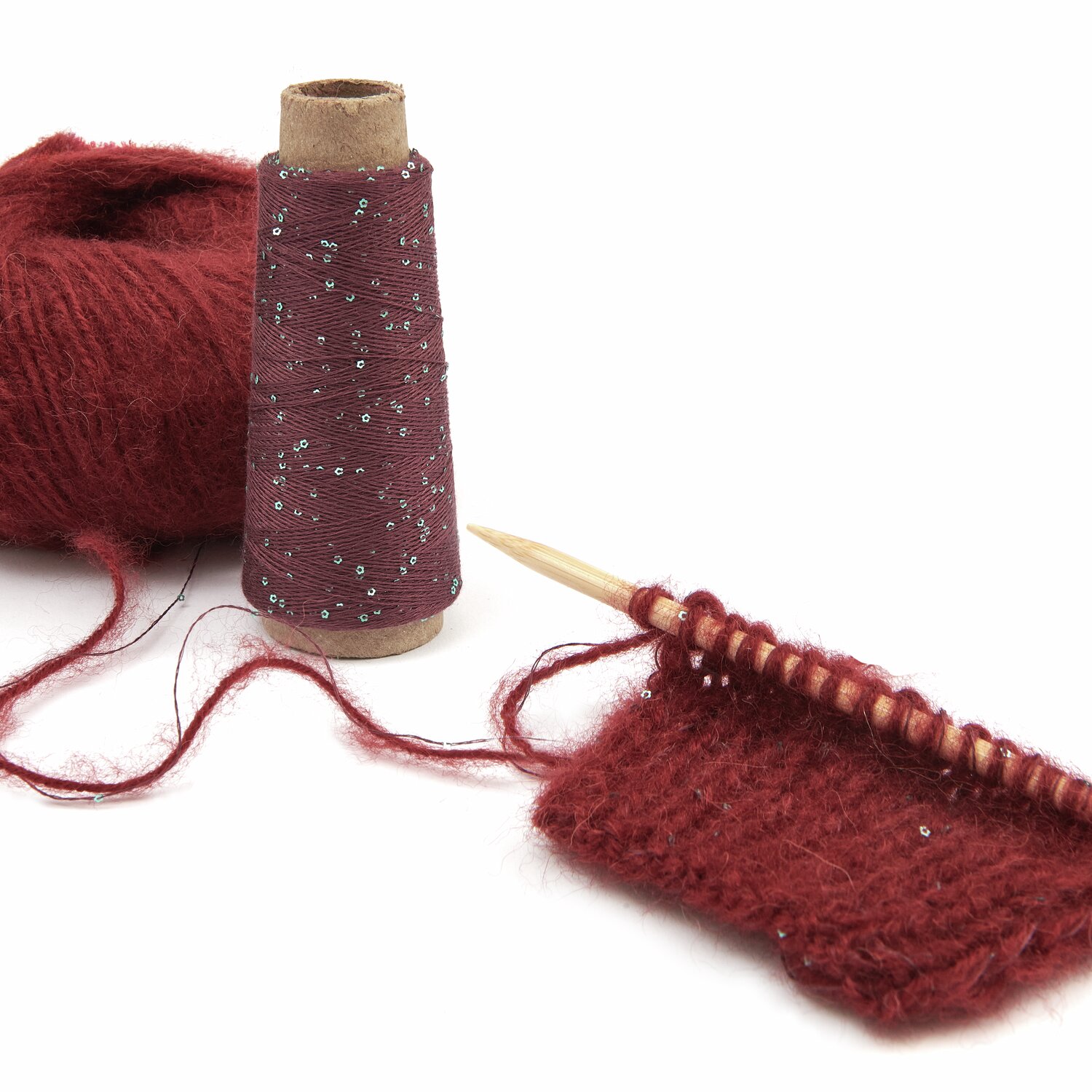 Lovewool No. 21 Herbst-Winter Sprachauswahl deutsch von Rico Design Rotes Strickgarn mit Glitzerfaden, auf einer Holzstricknadel gestrickt. Daneben eine Garnrolle. Perfekt für kreative Strickprojekte. Marke: Unbekannt.