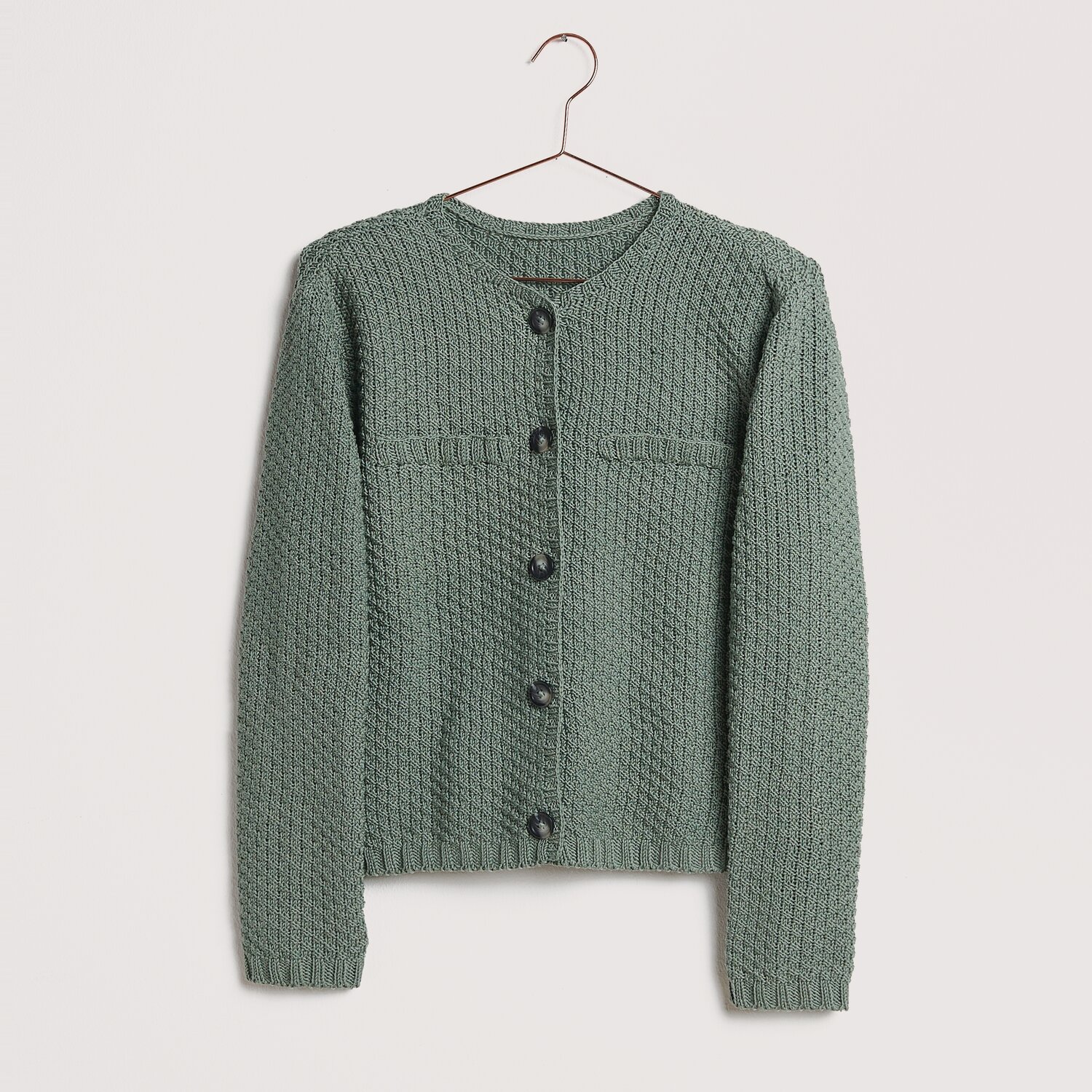 Die Neue Masche No. 12 Frühjahr-Sommer von idee. Creativmarkt Strickset Jacke Modell 18 aus Die Neue Masche No. 12, in Salbei, auf einem Kleiderbügel präsentiert.