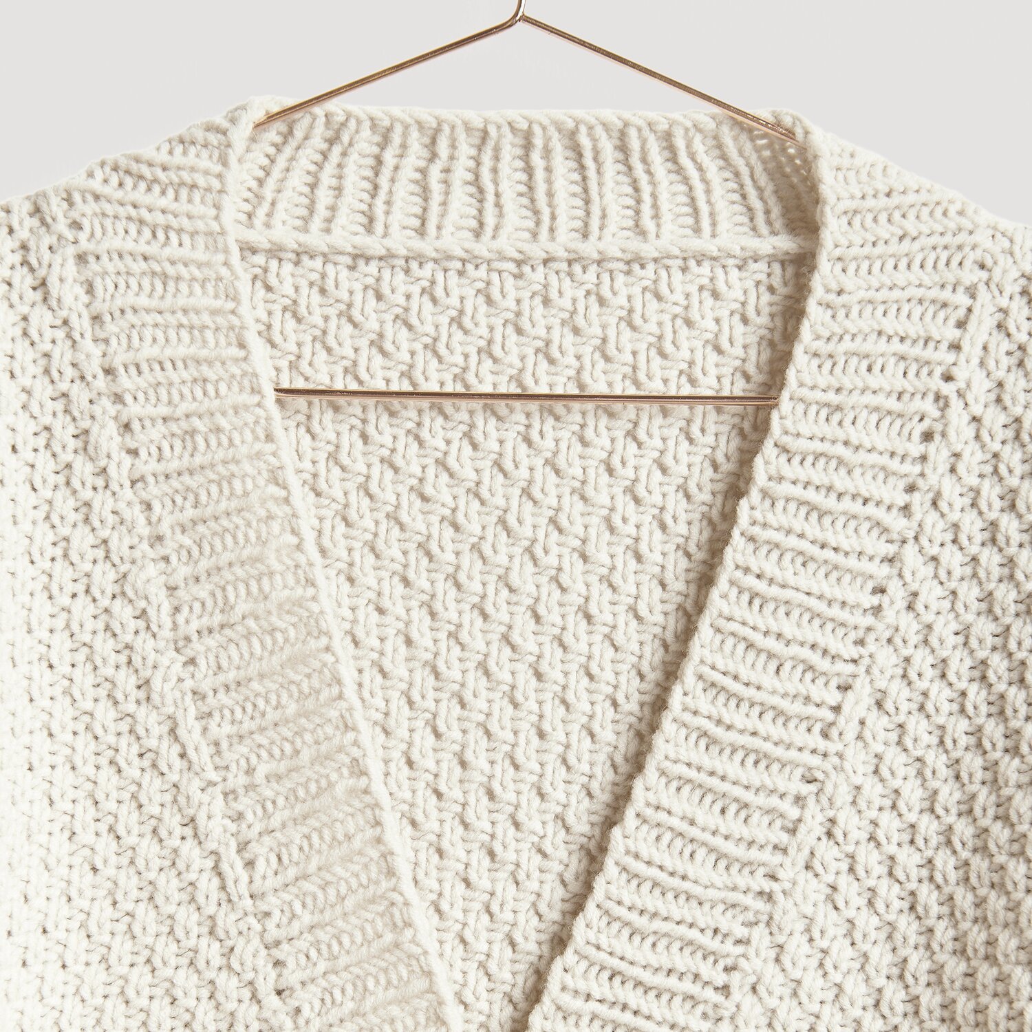 Die Neue Masche No. 13 Herbst von idee. Creativmarkt Die Neue Masche No. 13 Herbst: Cremefarbener Strickpullover mit Zopfmuster, präsentiert auf einem Kleiderbügel.