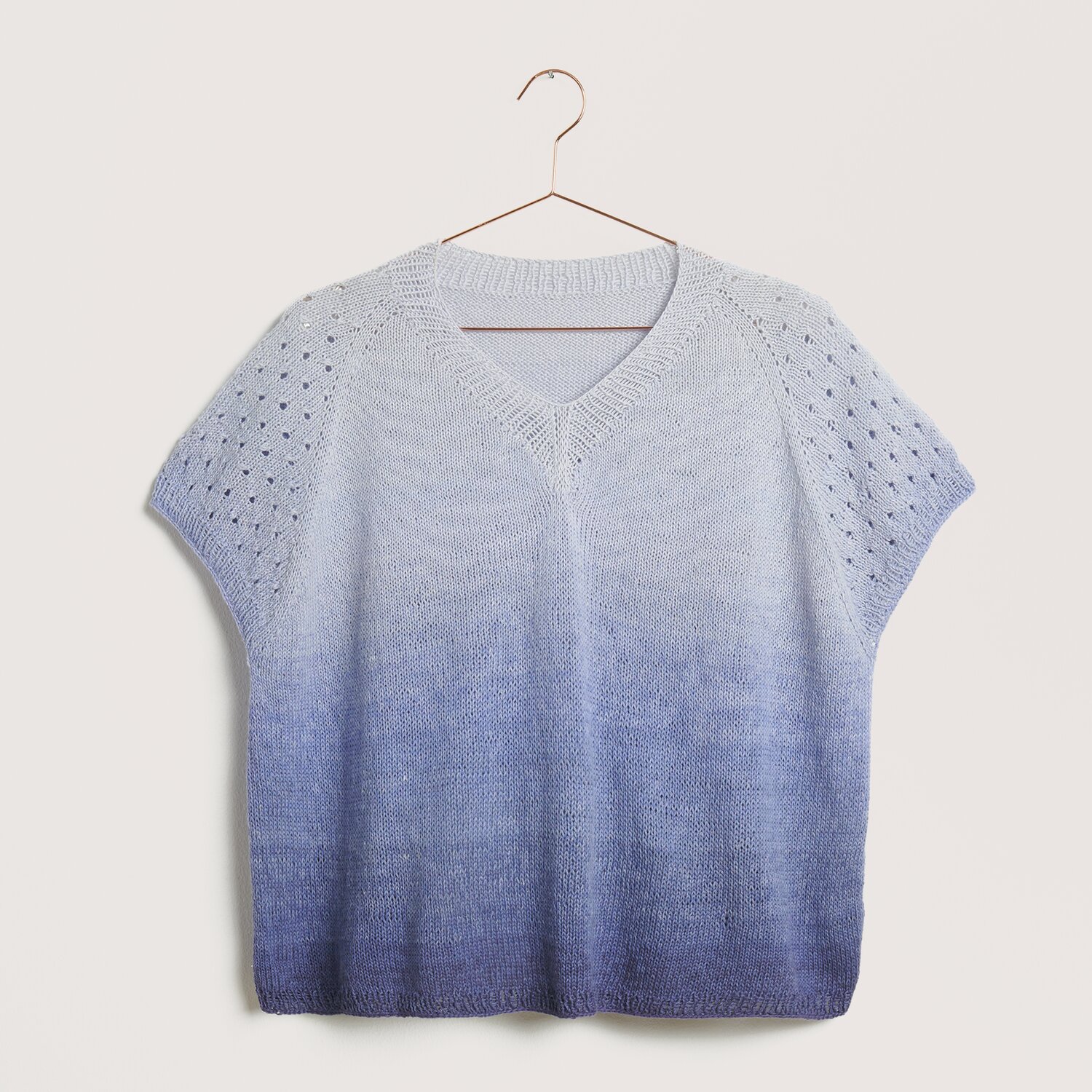 Strickset Top Modell 24 aus Die Neue Masche Nr. 9, blaues Oberteil mit V-Ausschnitt und Lochmuster, aufgehängt an einem Kleiderbügel.