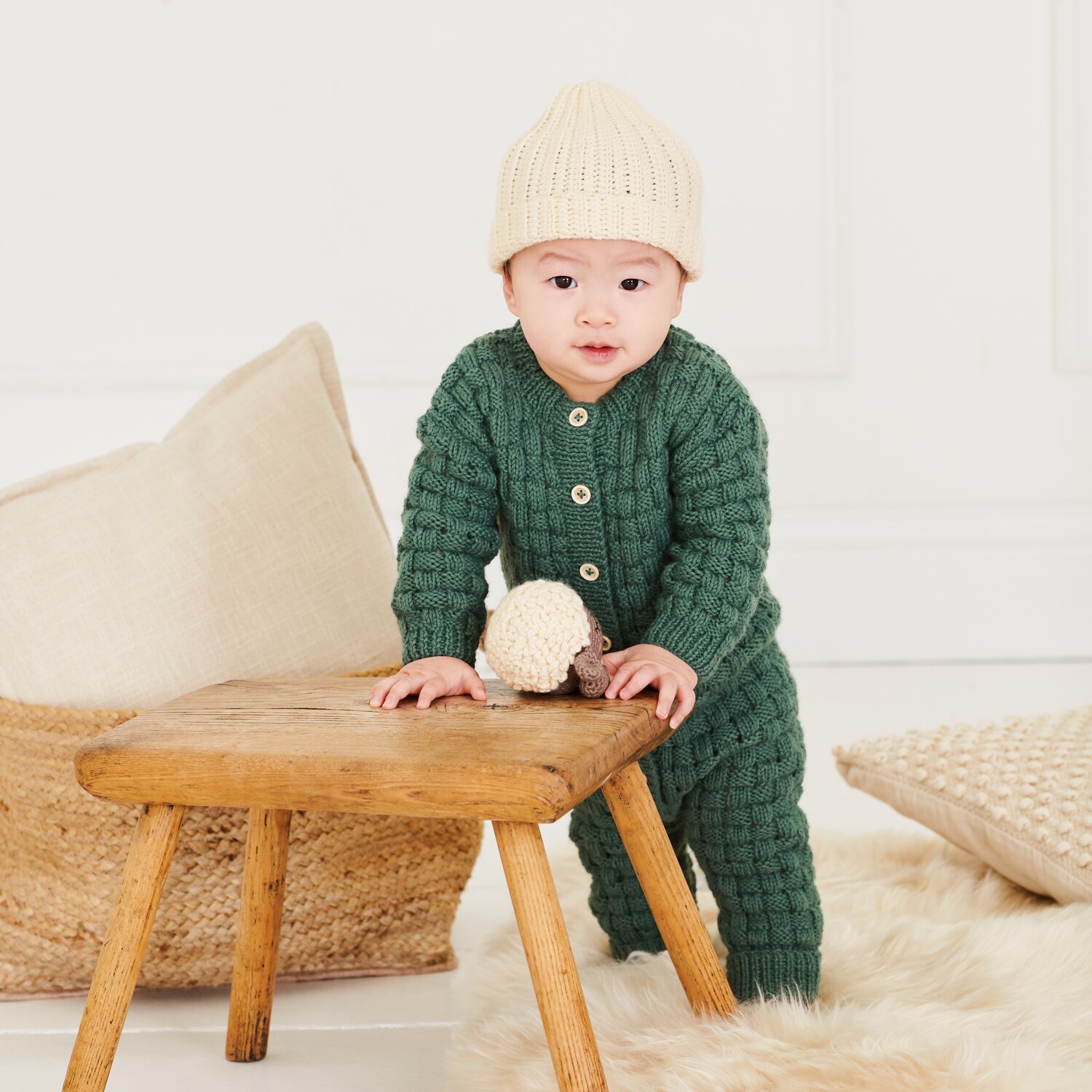 Strickset Strampler Modell 19 aus Baby 044, gemütlicher Einteiler mit Strukturmuster, getragen von Kleinkind vor Hocker in skandinavischer Wohnatmosphäre